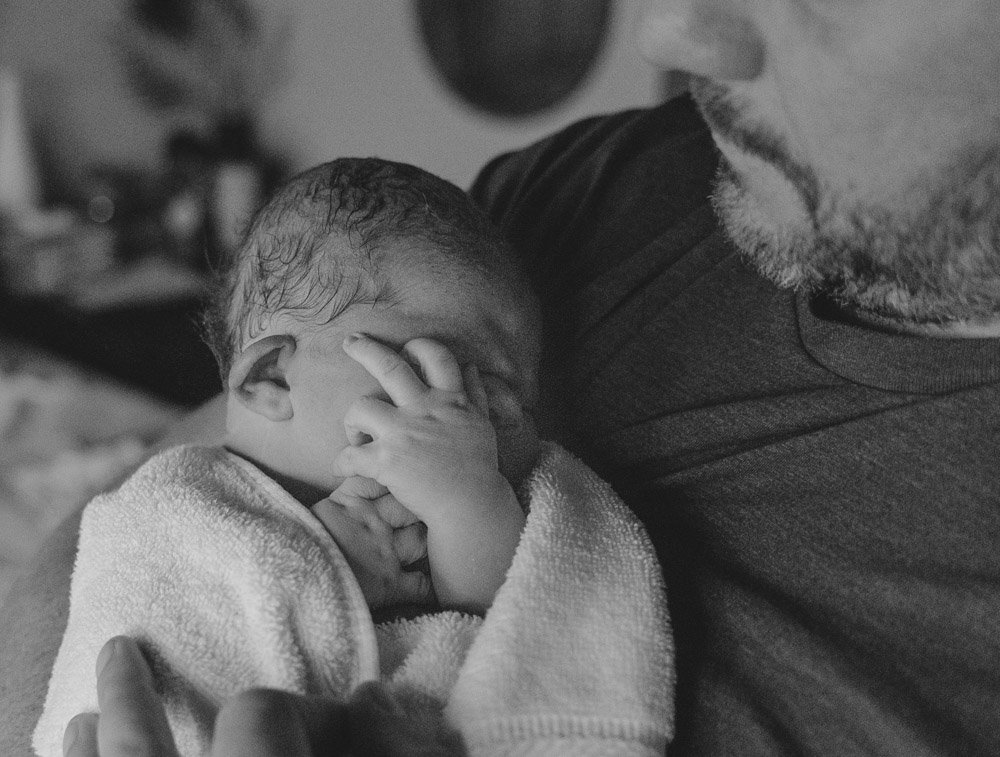 A man holding a sleeping baby in a towel, close-up of their faces in black and white.