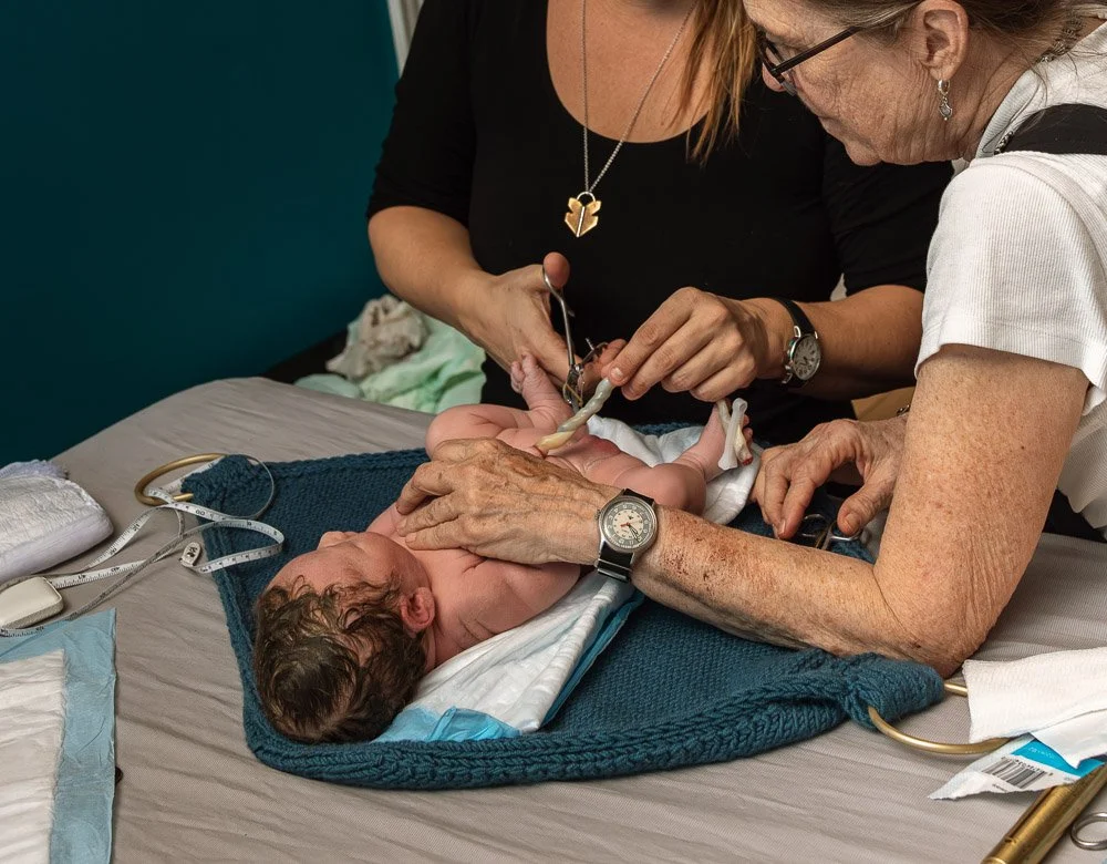 A newborn baby is being cared for by two women, one possibly a nurse or caregiver, in a hospital or medical setting.