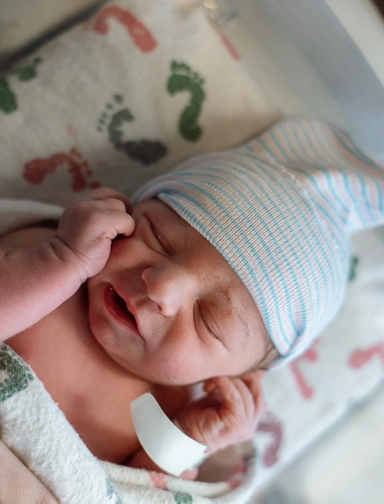 Close-up of a sleeping newborn baby wearing a striped hospital hat, lying on a blanket with colored question marks.