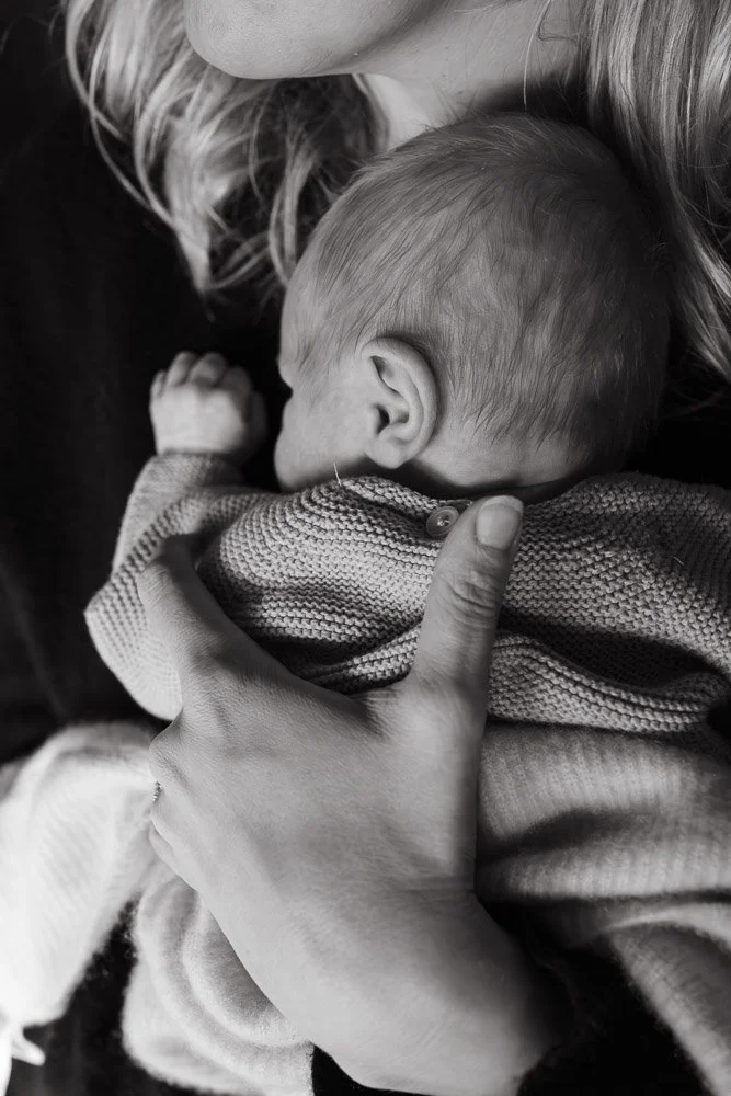 A person holding a sleeping baby close to their chest, with the baby leaning on the person's shoulder. The photo is in black and white.
