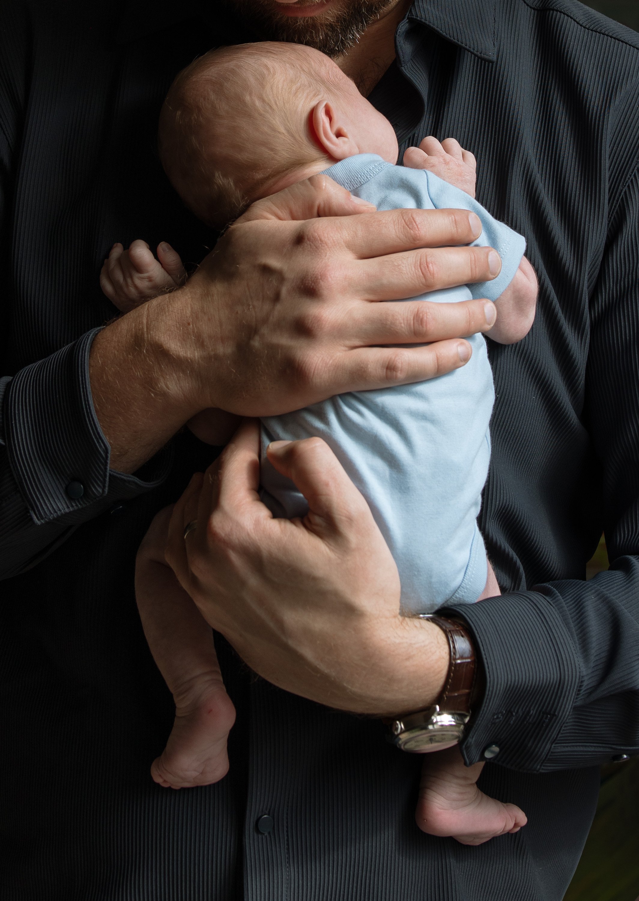a dad holds a newborn baby boy against his chest during an in home newborn lifestyle session in Westlake, photo captured by Austin in home newborn photographer Hailey Copland 