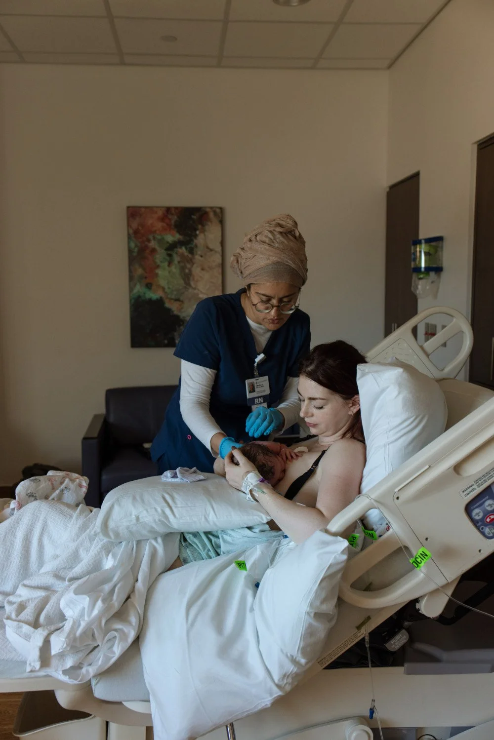 A lactation consultant  attending a postpartum mom in a hospital room, holding her newborn baby after childbirth, helping her learn how to breastfeed.