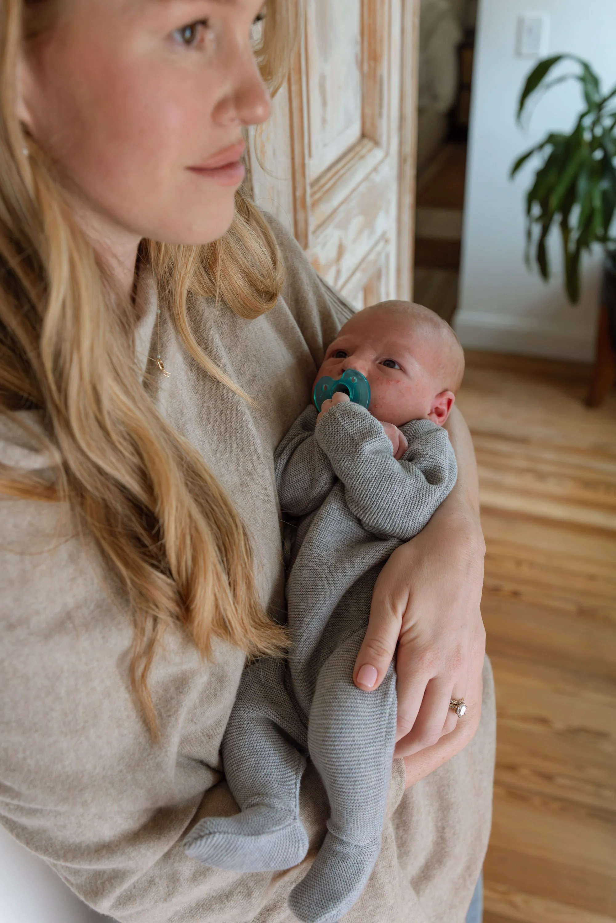 A woman holding a baby with a pacifier in their mouth, both sitting indoors.