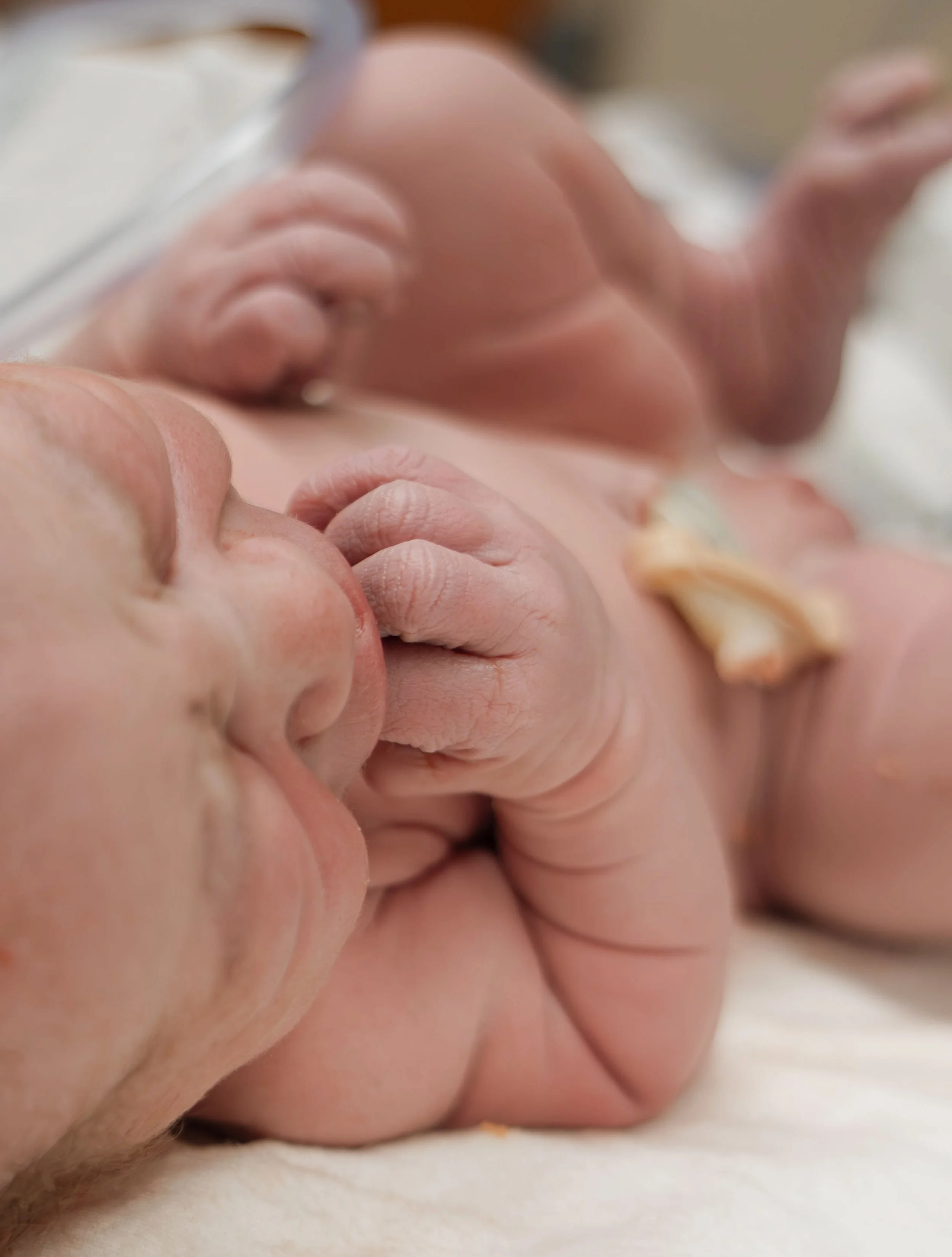 Close-up of a newborn baby lying on a soft surface, holding its hand with its fingers near its face, with delicate skin and tiny features.