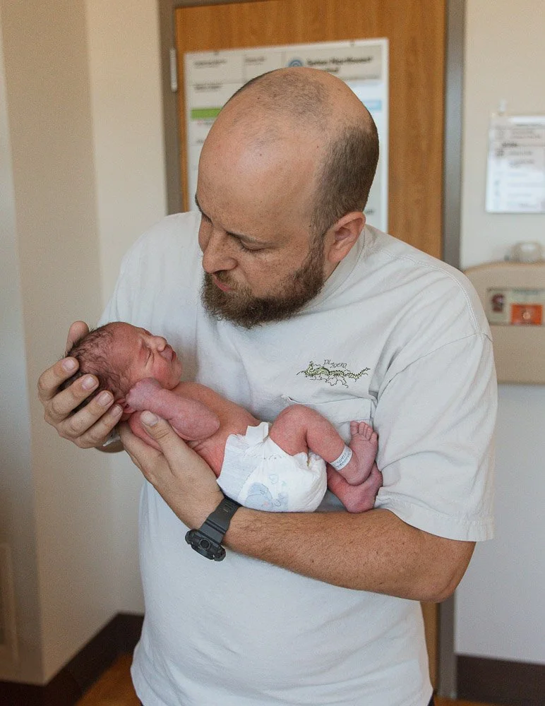 A man holding a newborn baby in a hospital room in Austin Texas