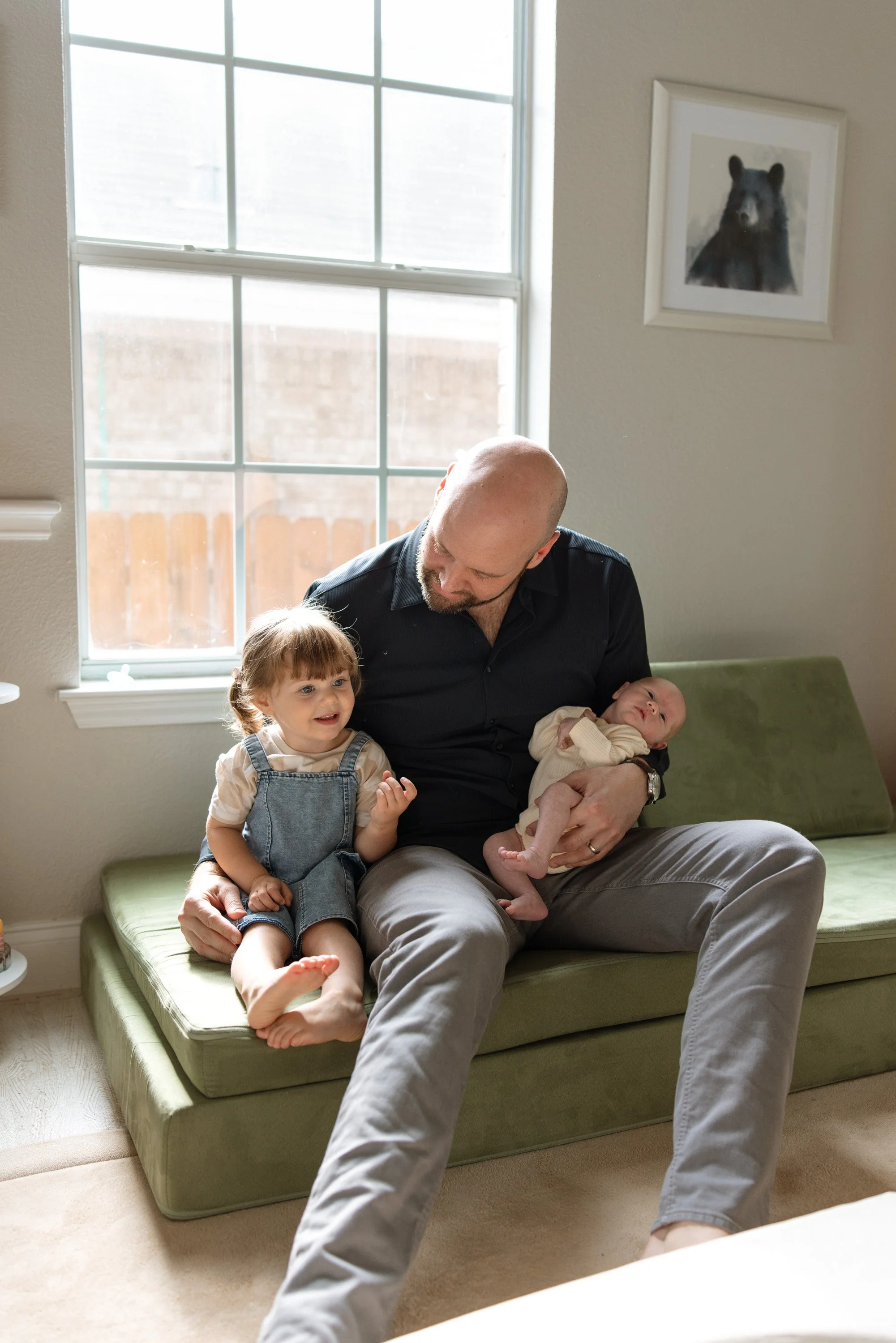 a dad sits with his daughter and newborn son during an in home newborn session, photo captured by Austin in home newborn photographer Hailey Copland 