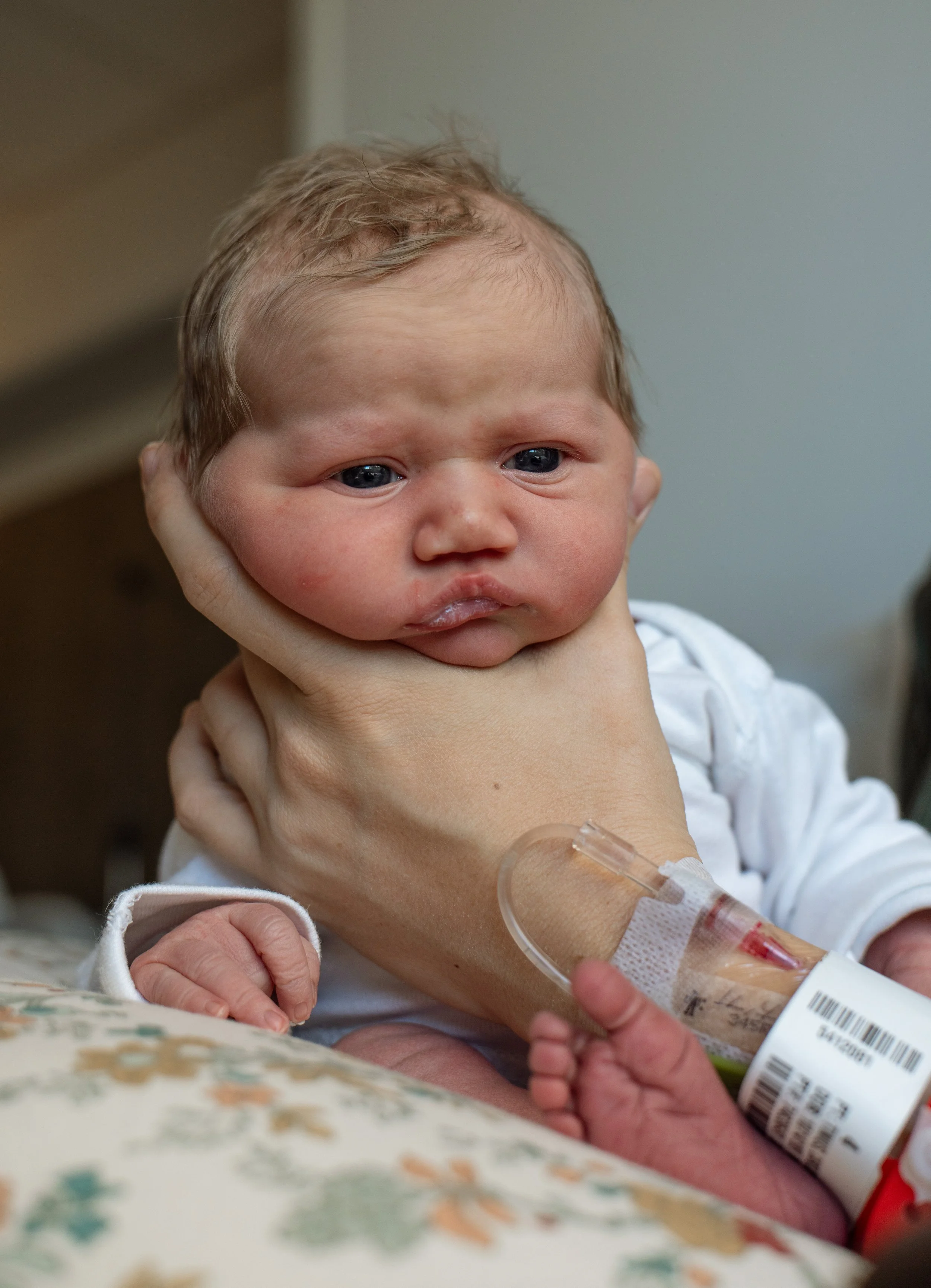 Austin Texas free 48 photograph of a newborn baby held by mom in a hospital setting wearing only a plain white onesie. 