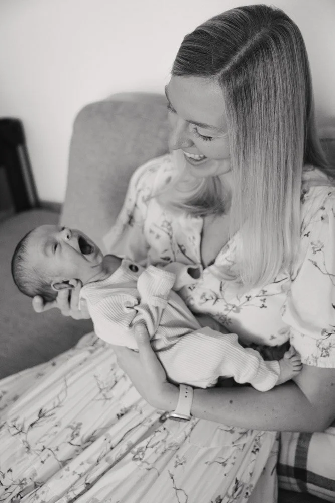 A woman holding a laughing baby on her lap, sitting on a couch, in black and white.