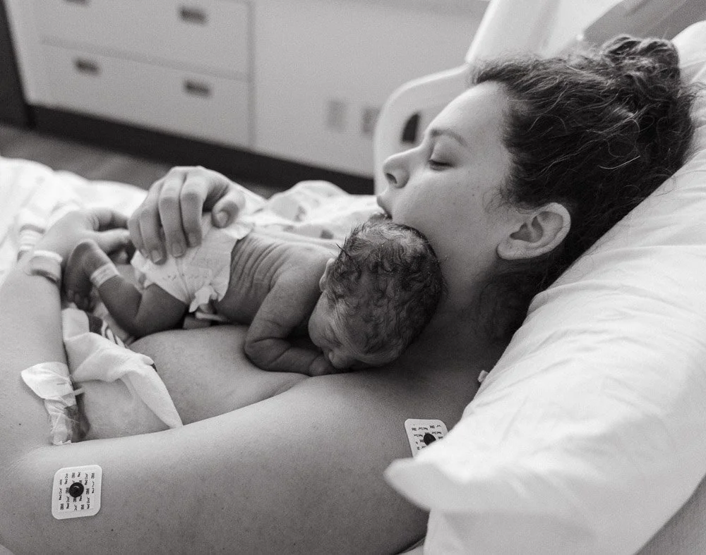 A woman lying in a hospital bed holding a newborn baby close to her chest.
