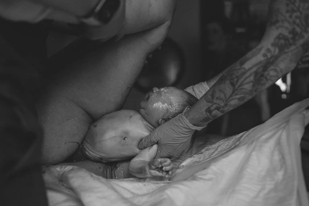 A newborn baby is being held by a healthcare professional during birth, with the baby lying on a cloth and the professional wearing gloves.