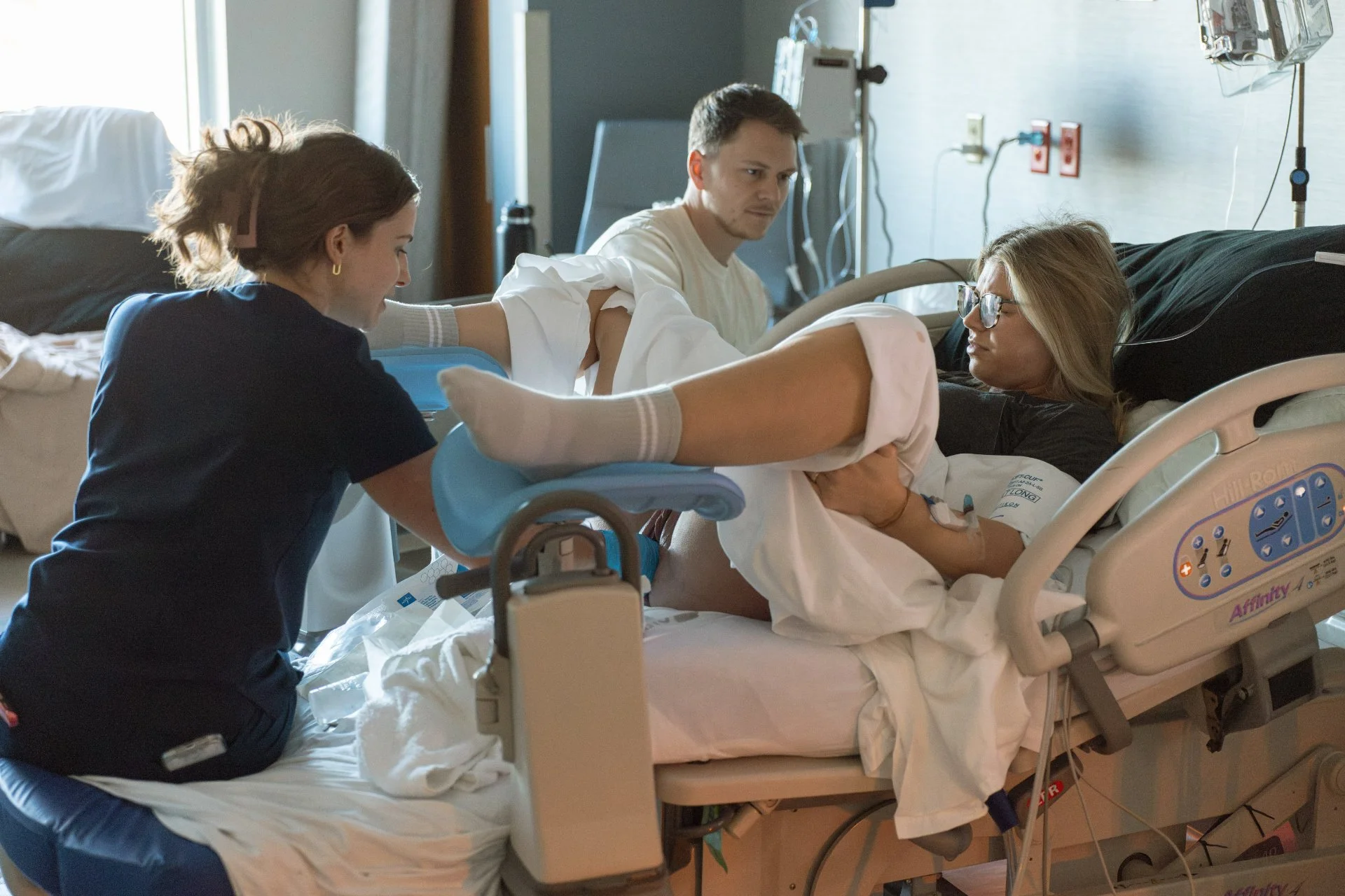 Natural light documentary birth photograph by an Austin birth photographer, mother in the hospital setting with a nurse and her husband while pushing