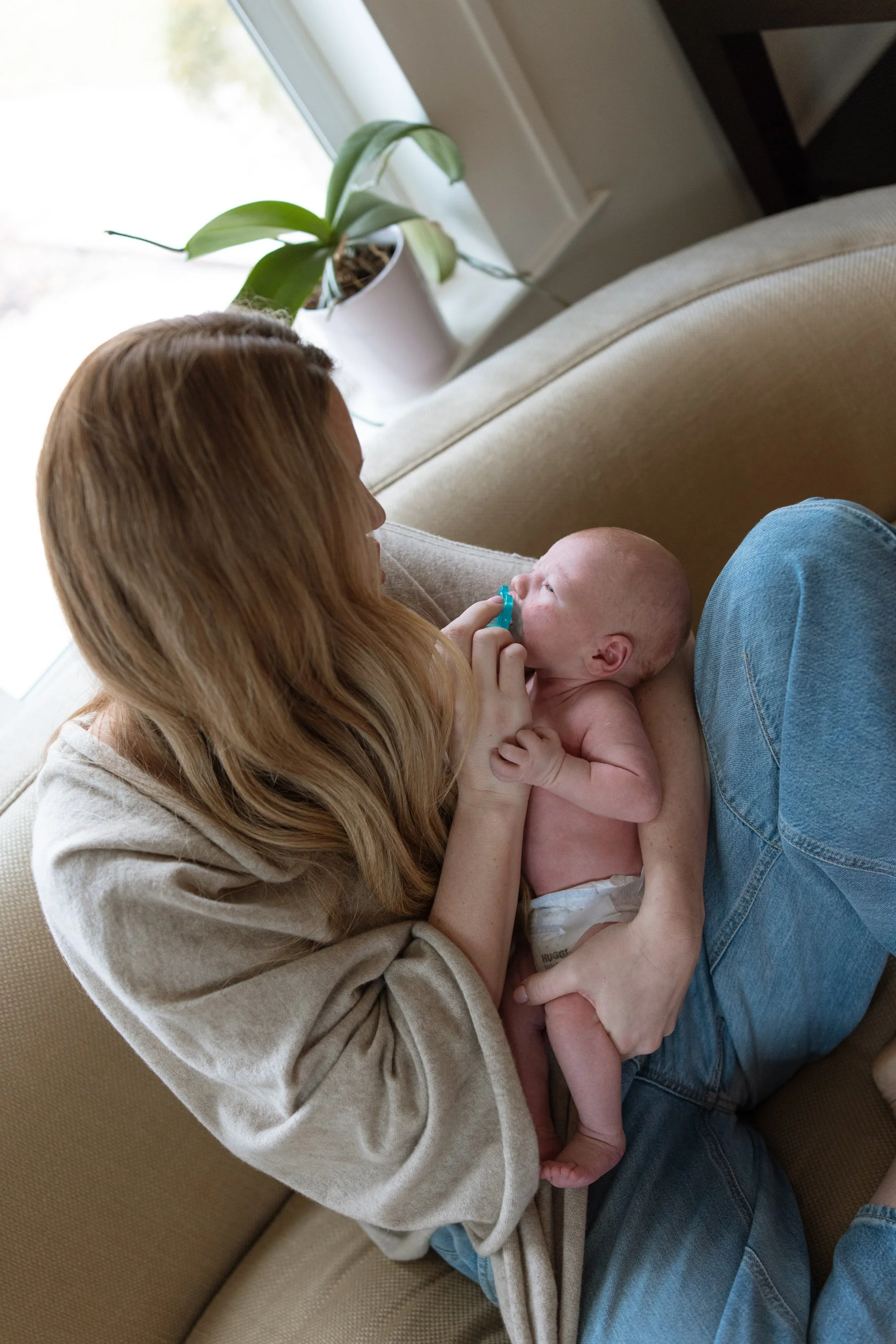 in home newborn photography session with a mom holding a newborn baby on her high end couch. 