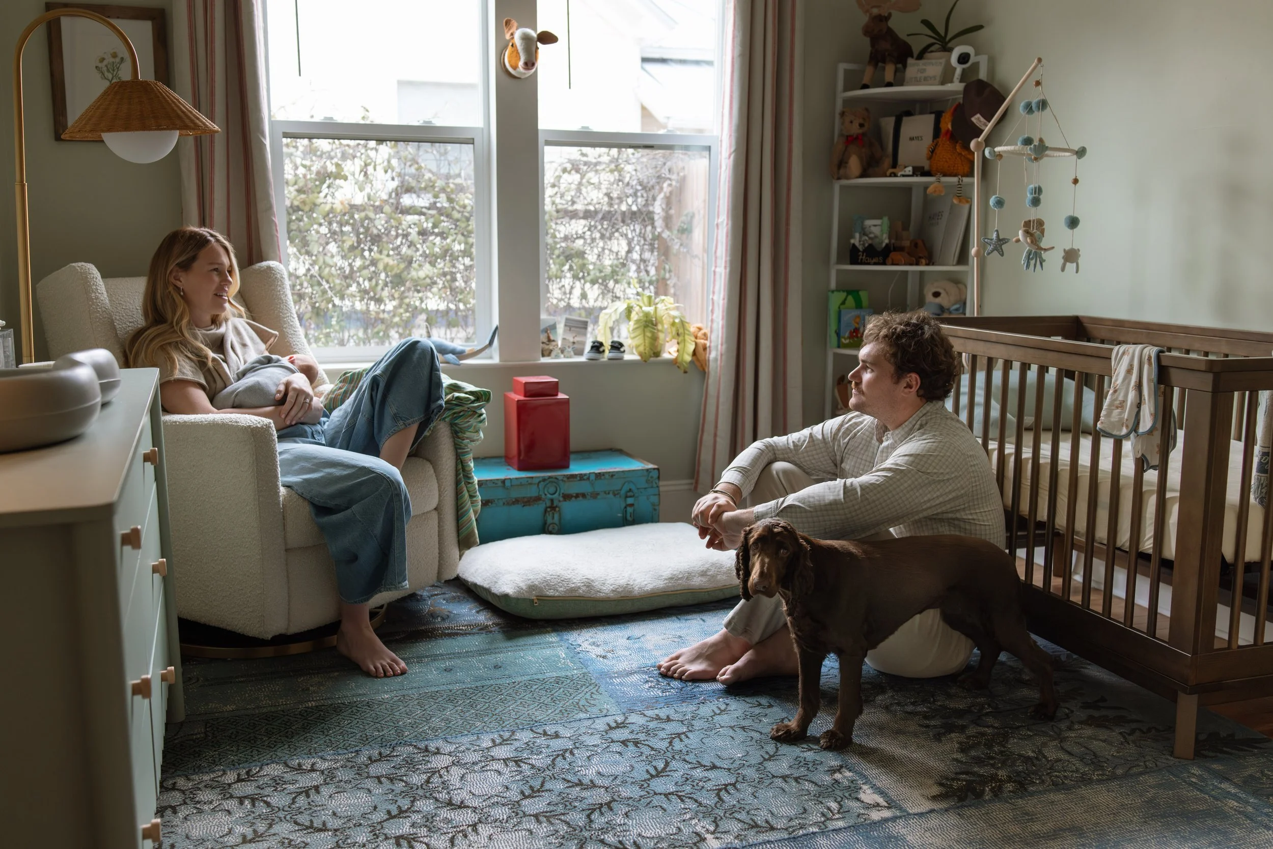 in home newborn session where mom, dad, and their dog sit in the baby's nursery while mom nurses the baby. 