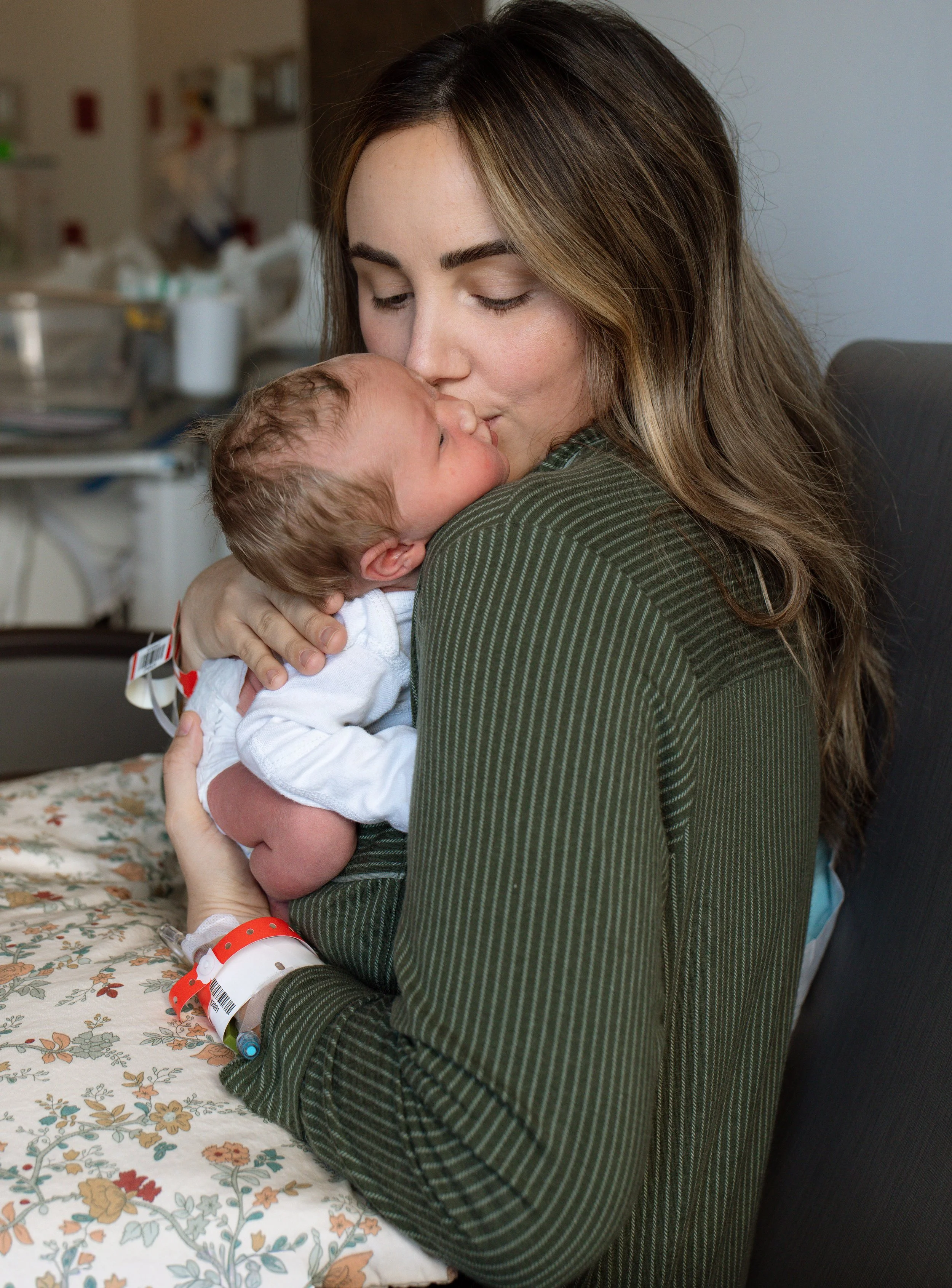 mom in hospital kissing a newborn baby that is placed over her shoulder and sleeping. 