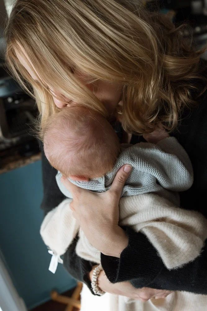 Woman with blonde hair kissing a baby on the head, holding the baby close.