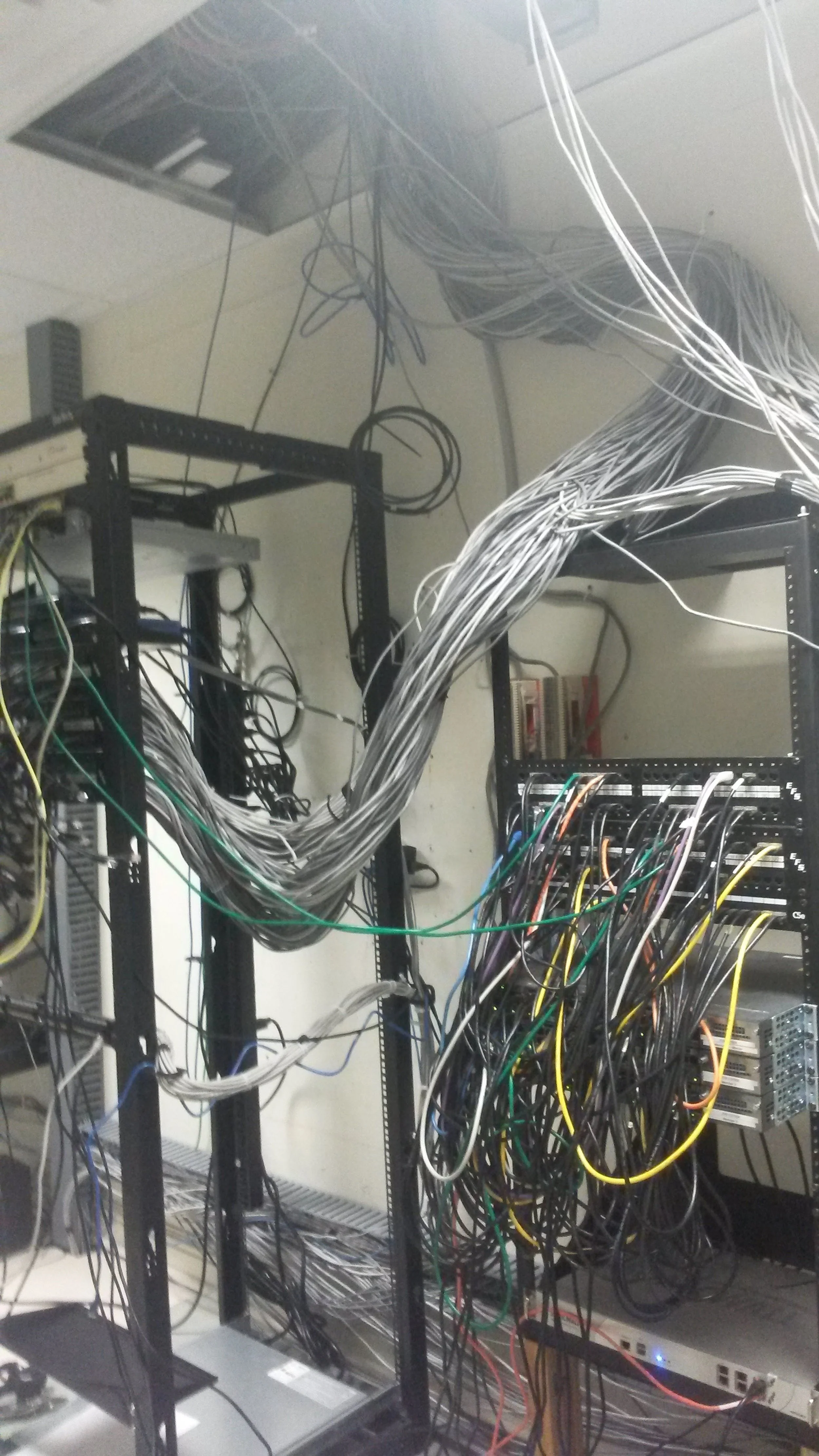 Server room with tangled network cables and open ceiling panel.
