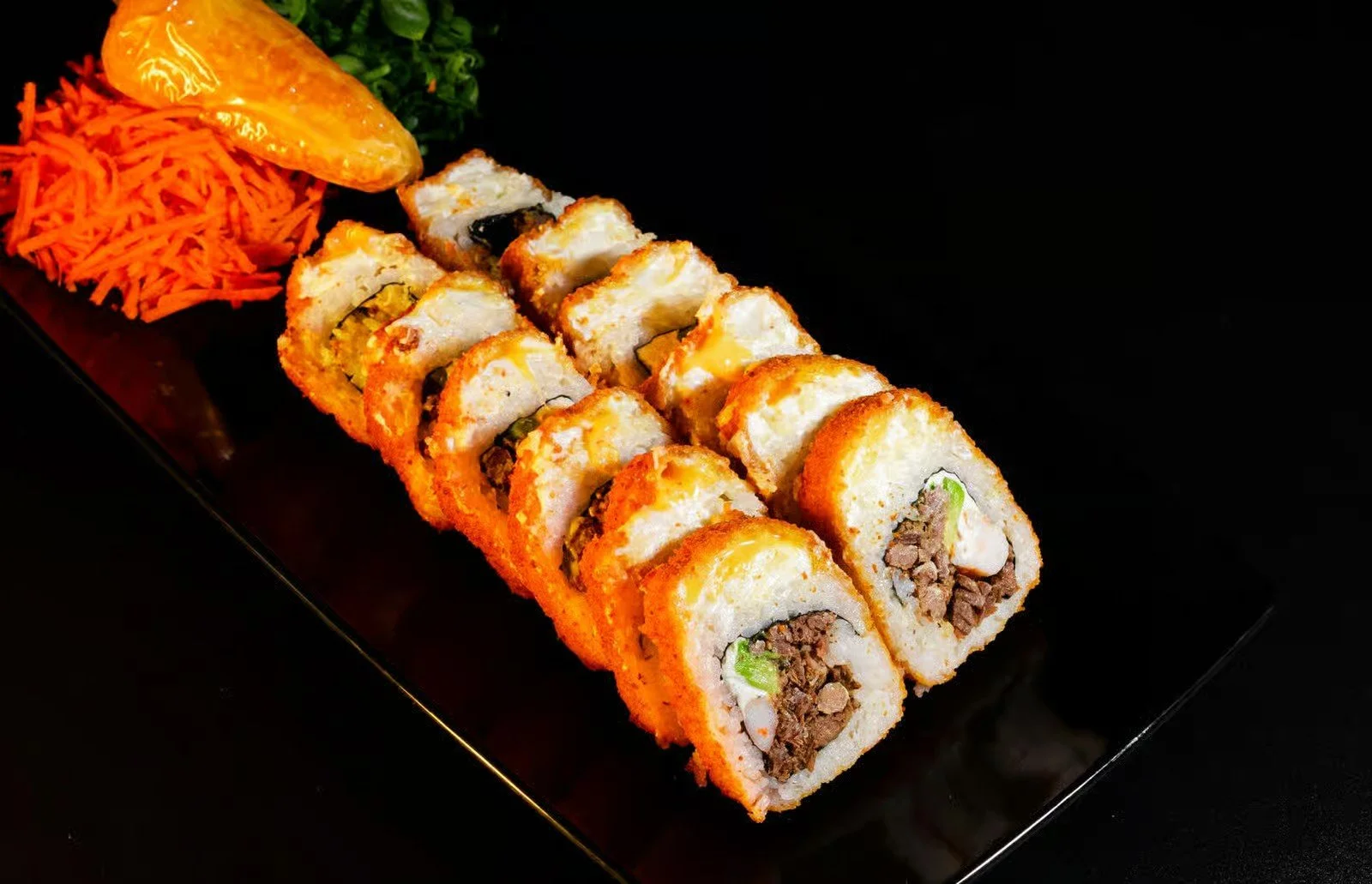 Sushi rolls arranged on a black plate with shredded carrots, a lemon wedge, and parsley garnish.