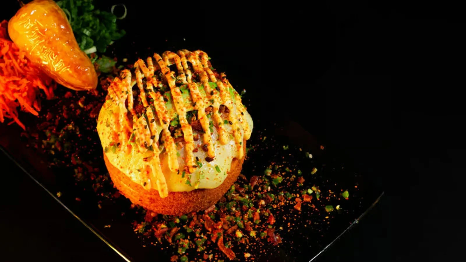 A gourmet dessert with a round base topped with ice cream, drizzled with sauces, garnished with herbs, and accompanied by a sauce and shredded garnishes on the side on a black plate.