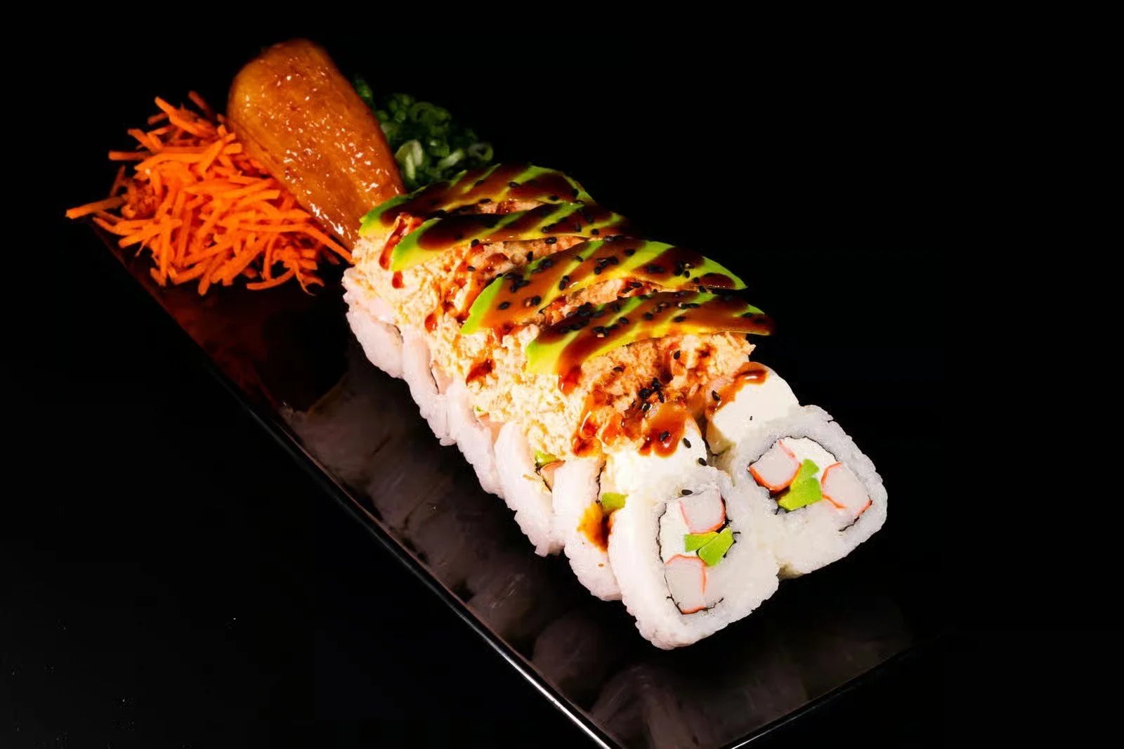 Sushi roll with avocado, crab, and fish, topped with sauce, served with pickled ginger, wasabi, and shredded carrots