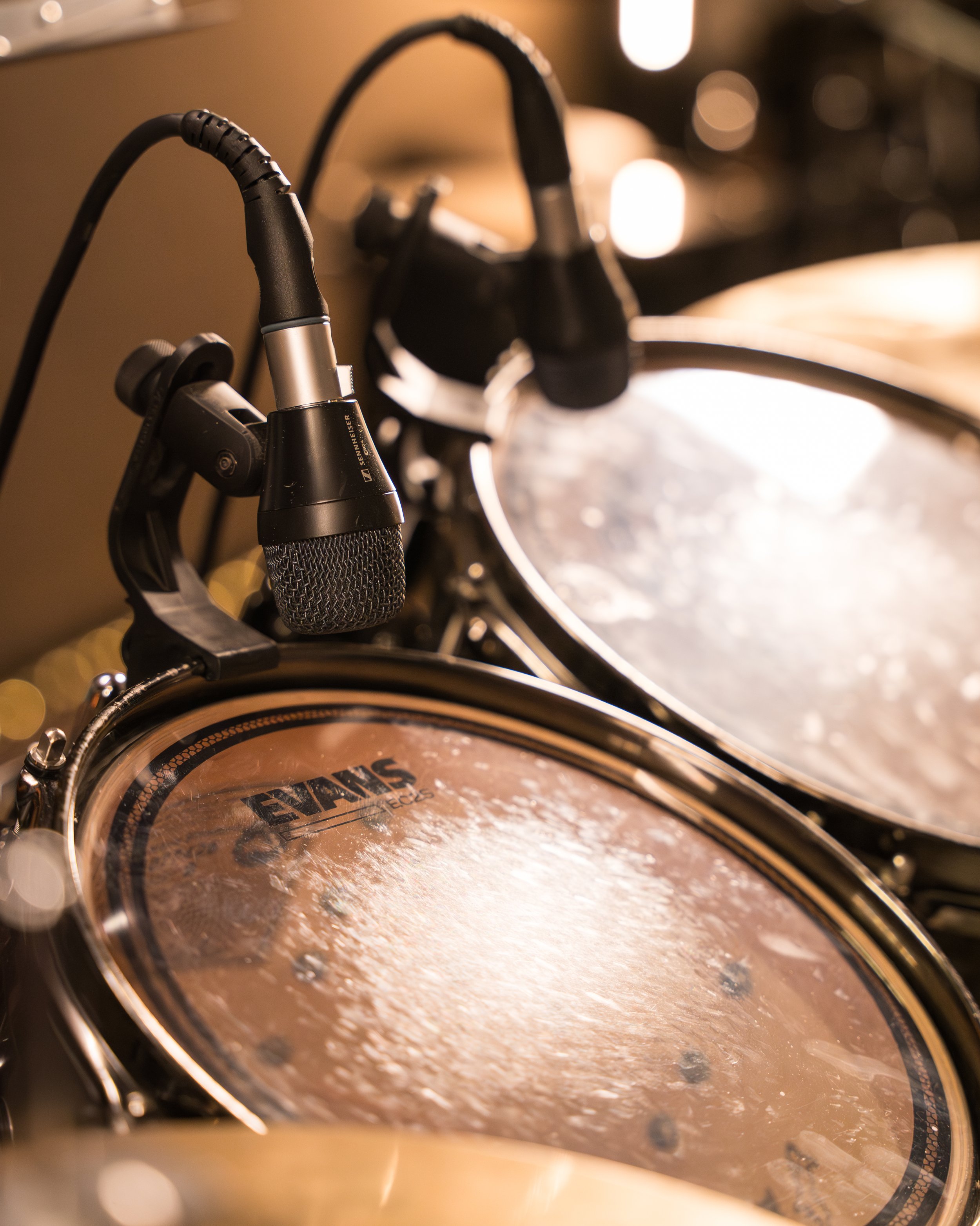 Close-up of a drum set with a microphone positioned above the snare drum, in a dimly lit room.