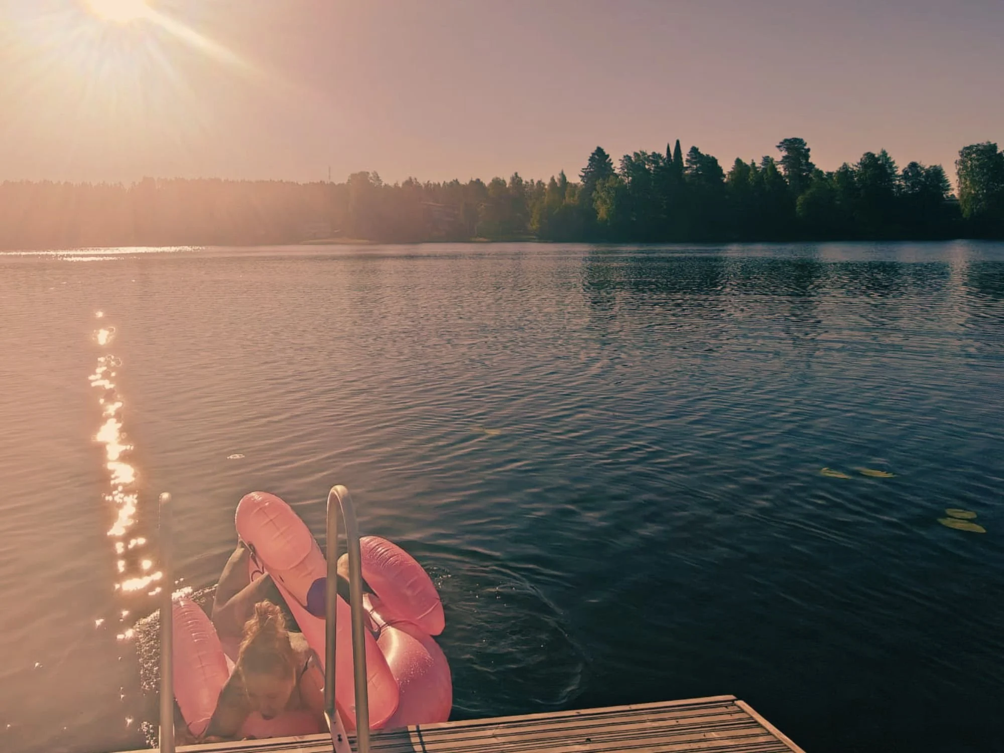 Kesäinen järvimaisema ja henkilö flamingo-uimalelun kanssa