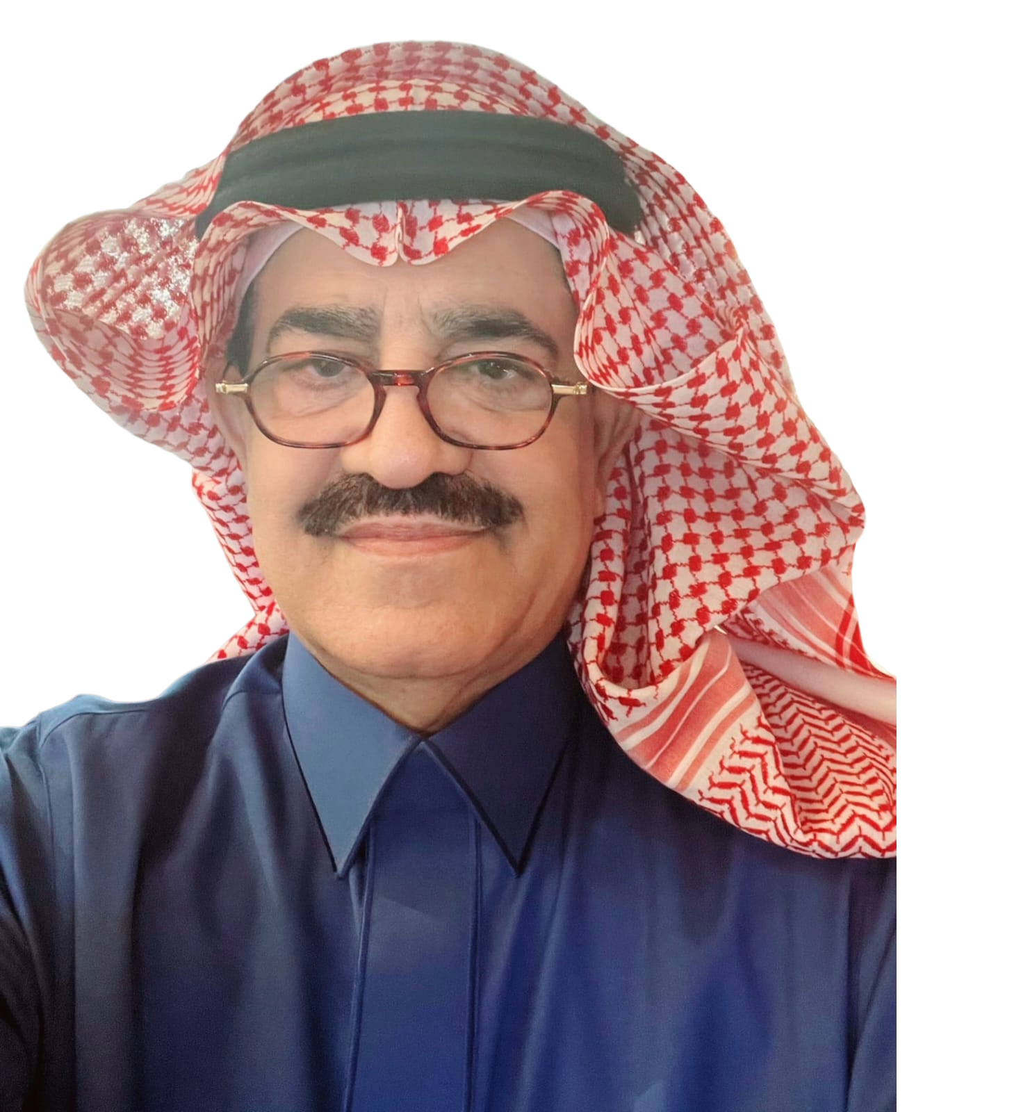 A man wearing traditional Middle Eastern attire, including a red and white checkered keffiyeh headscarf, glasses, a navy blue shirt, and a black agal, smiling for a selfie.