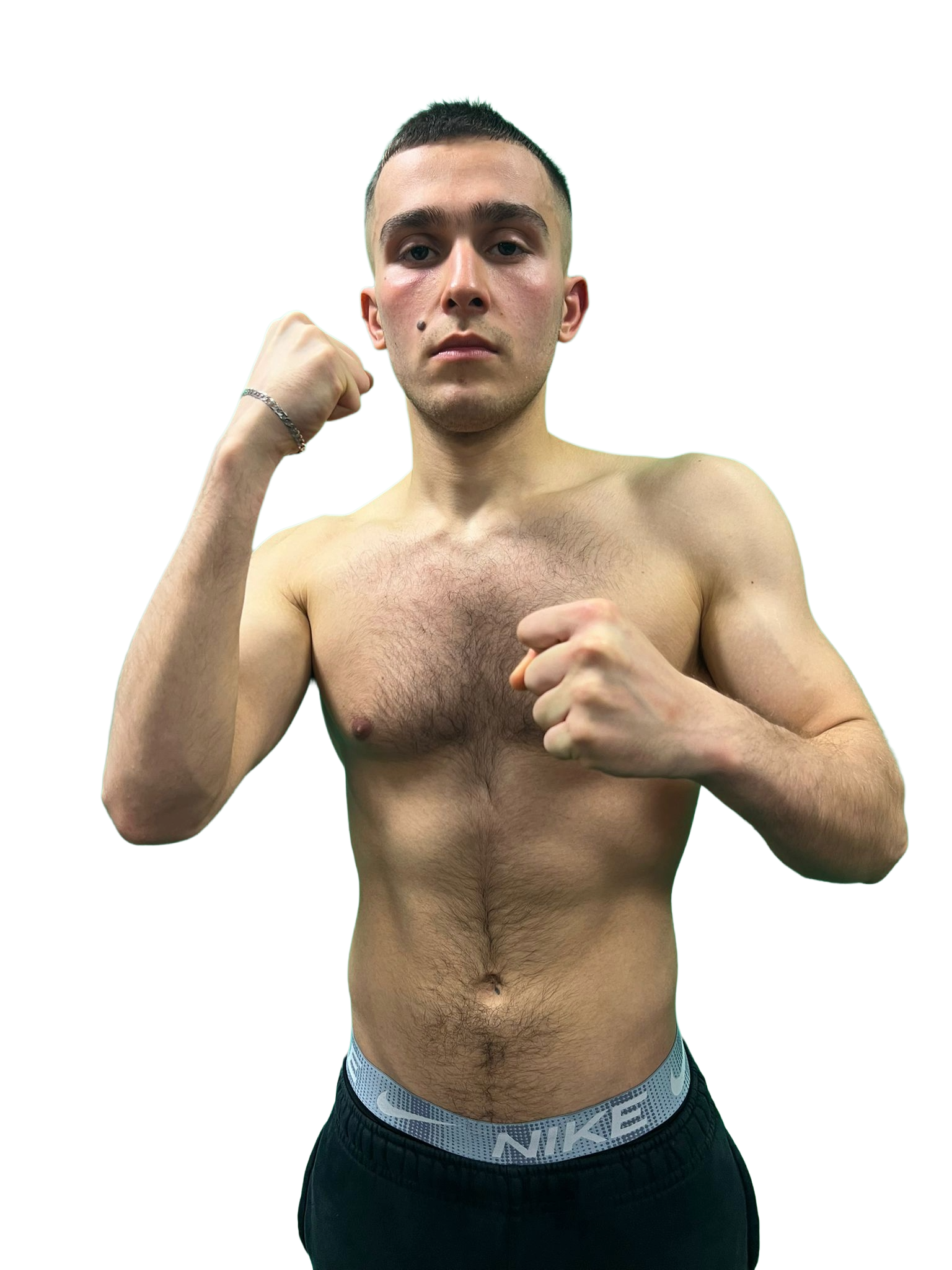 A middle-aged Black man with gray beard and short hair sitting on a bench in a beige room, wearing a brown polo shirt and light-colored pants, looking thoughtfully to the side.
