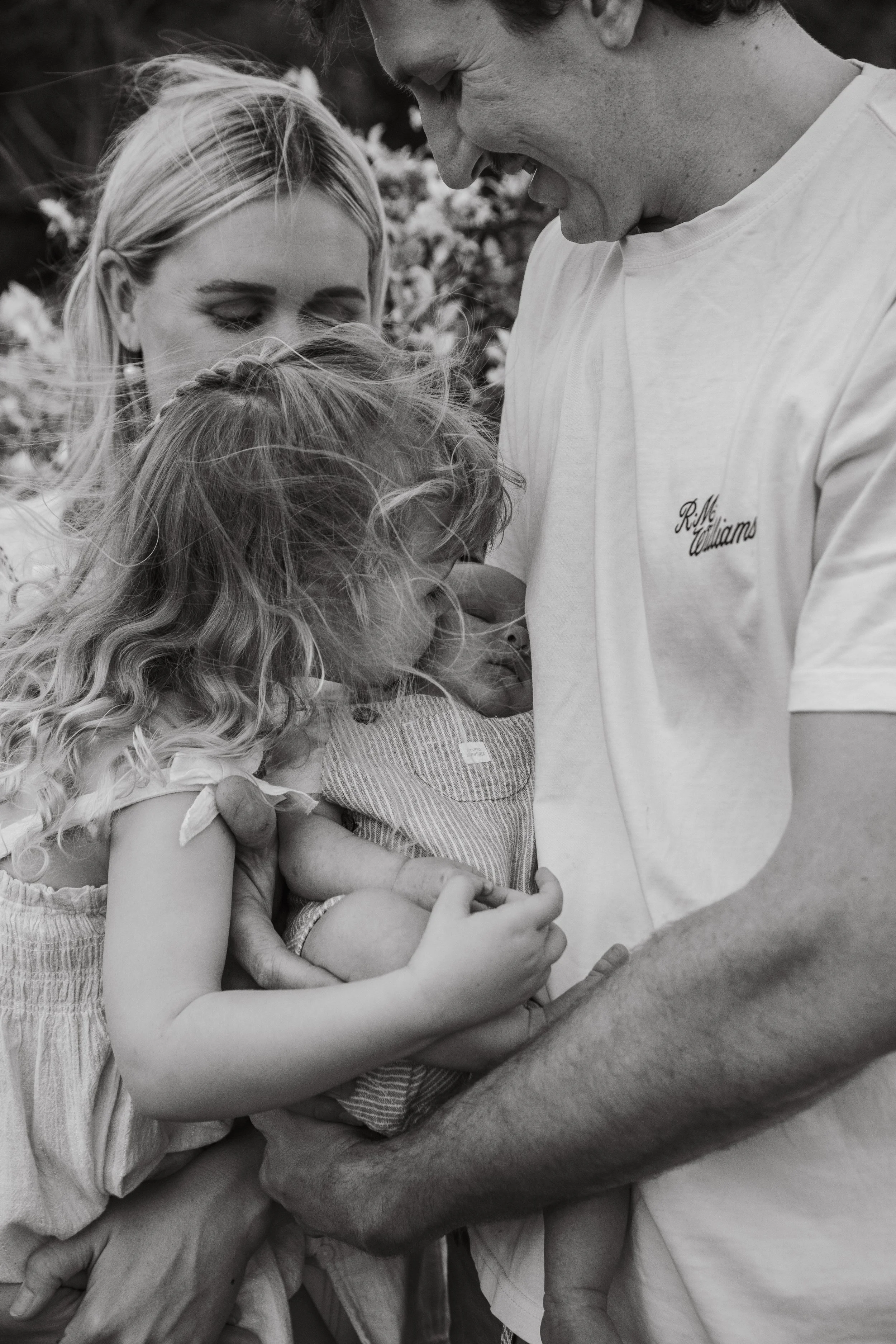 Black and white photo of a family holding a newborn baby, with two women and a man, all smiling and looking at the baby.