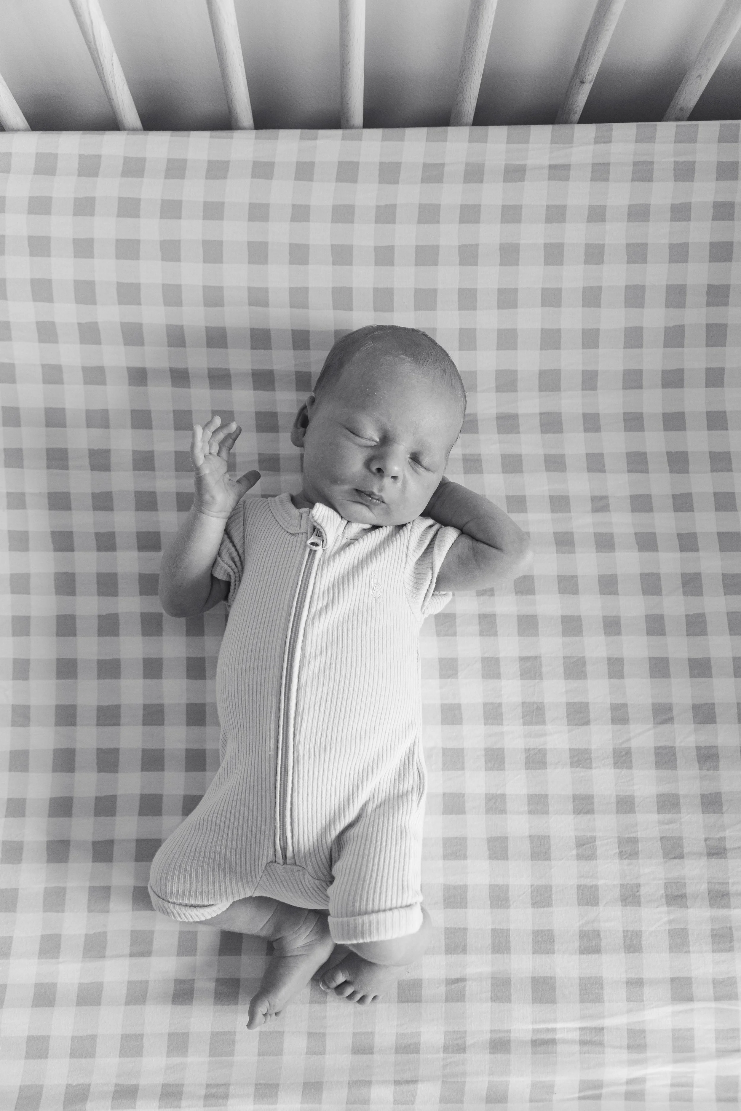 A sleeping newborn baby lying on a checkered pillow in a crib.
