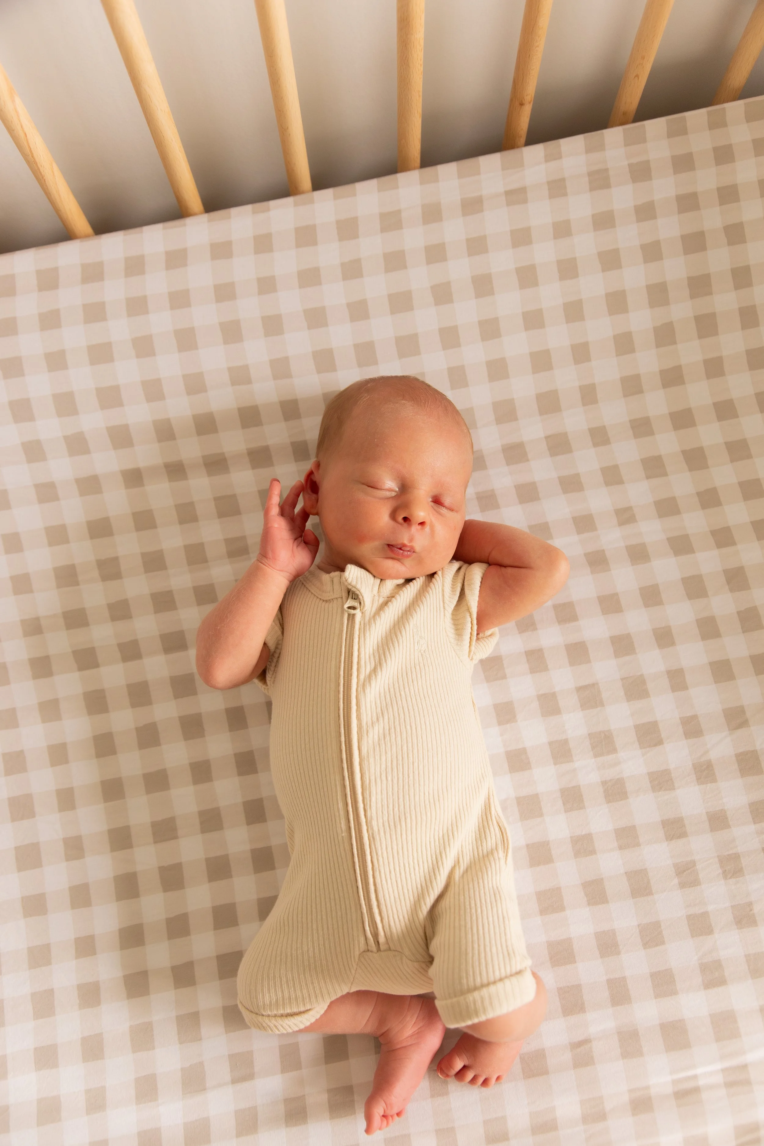 Newborn baby sleeping on a checkered beige and white blanket.