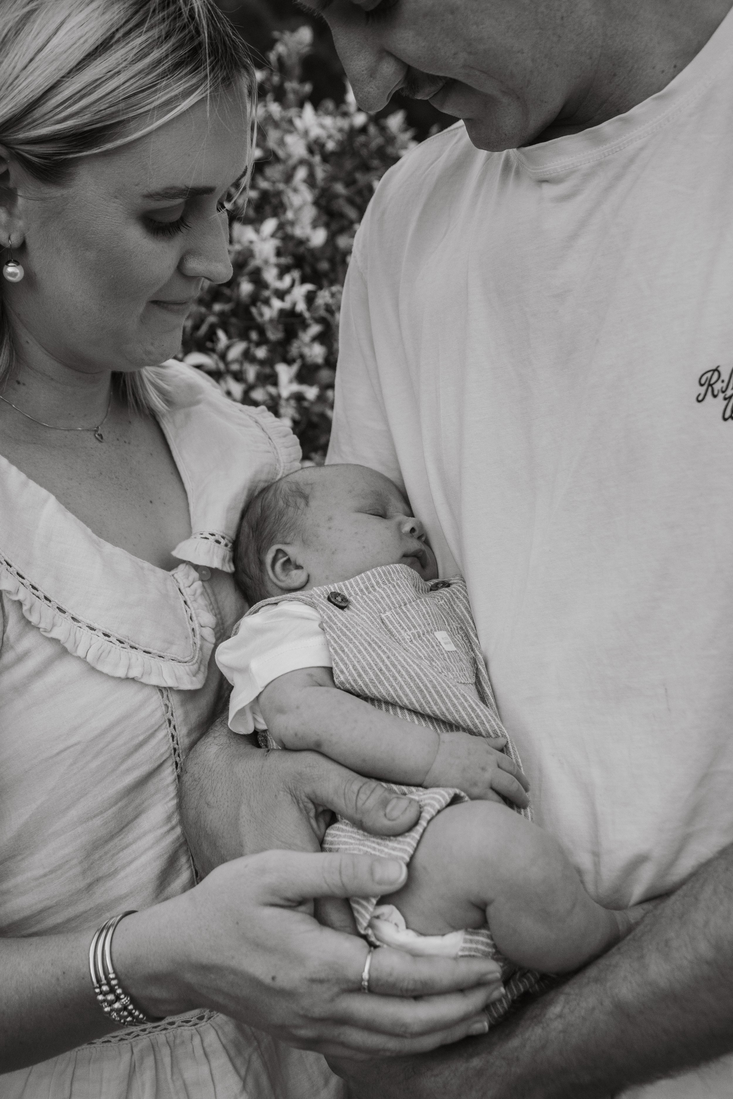 A black and white photo of a newborn baby being held by a woman while a man looks on lovingly.