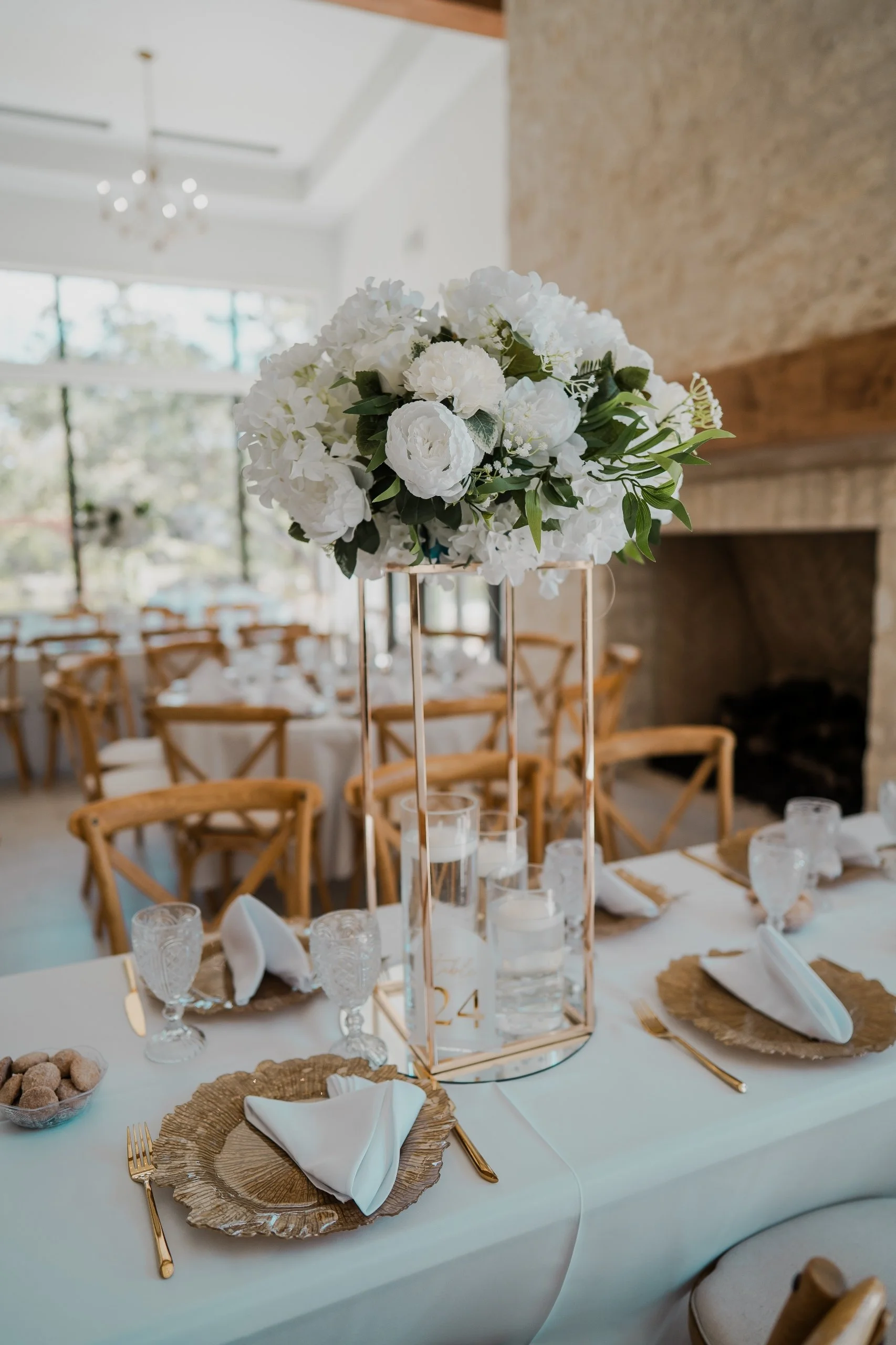 Elegant tablescape with white floral centerpiece, gold accents, water glasses, candles, and folded napkins at a formal event venue.