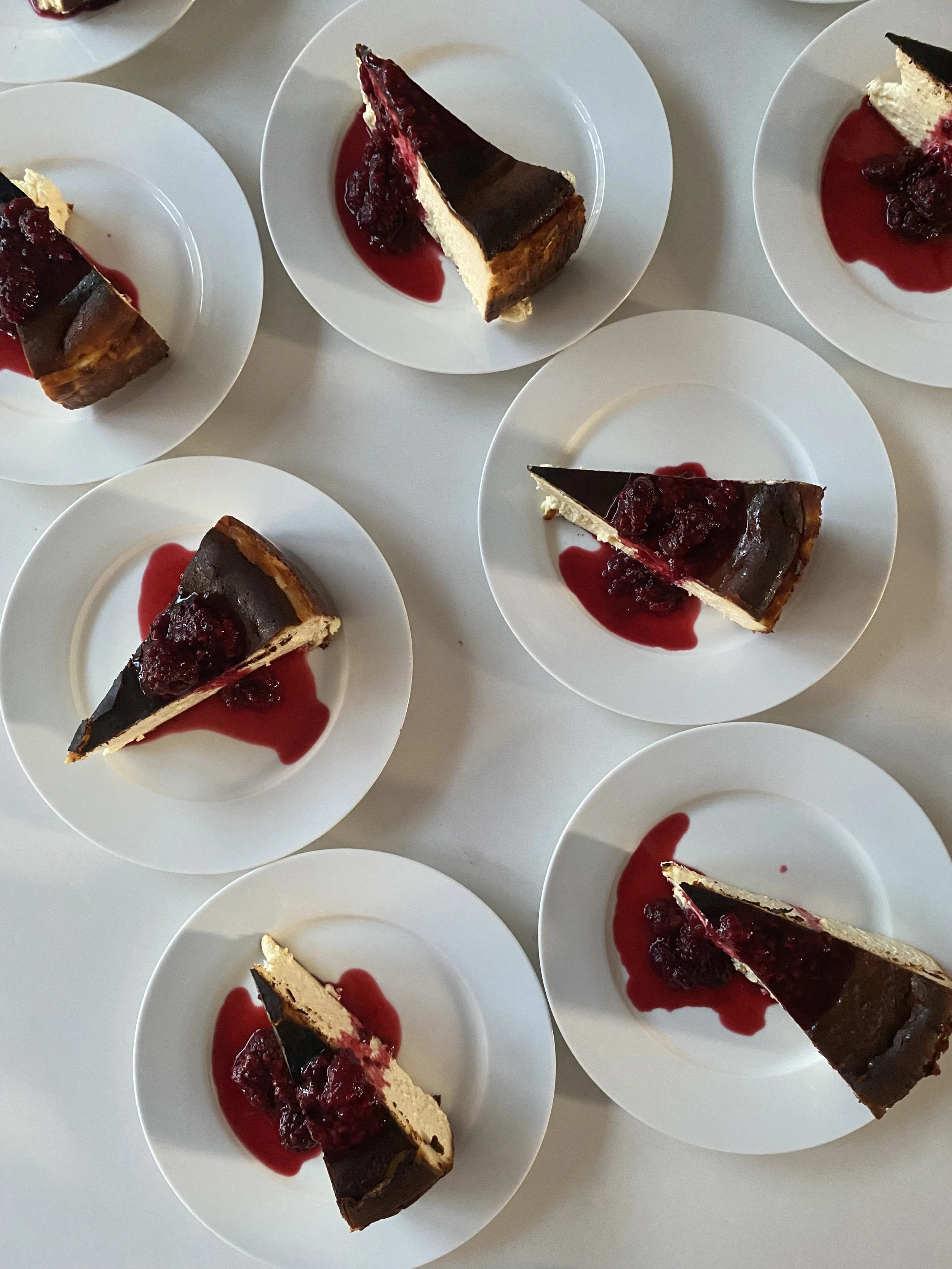Multiple slices of burnt Basque cheesecake with a cherry sauce on white plates.