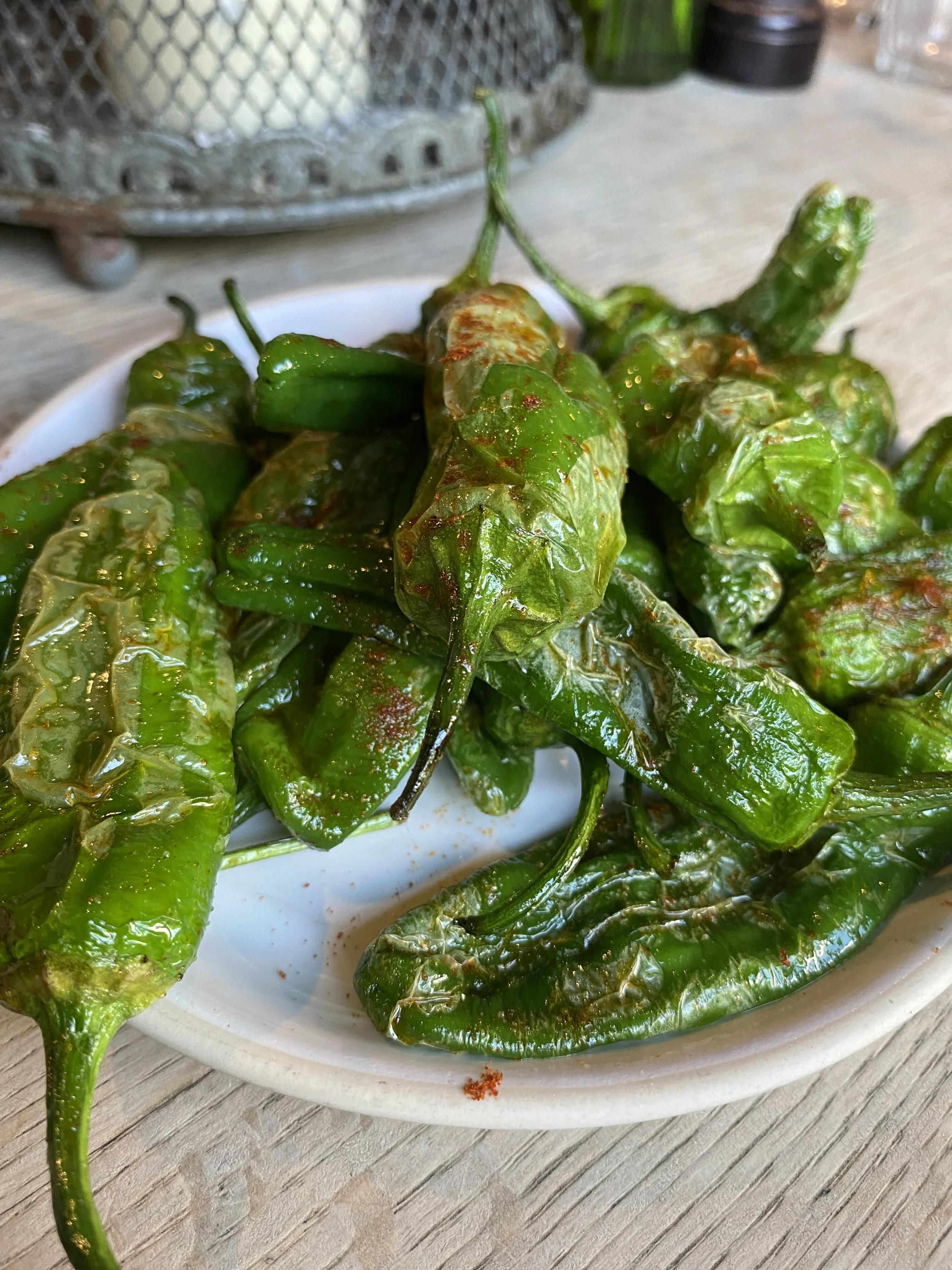 A white oval dish filled with roasted green chili peppers on a wooden surface.