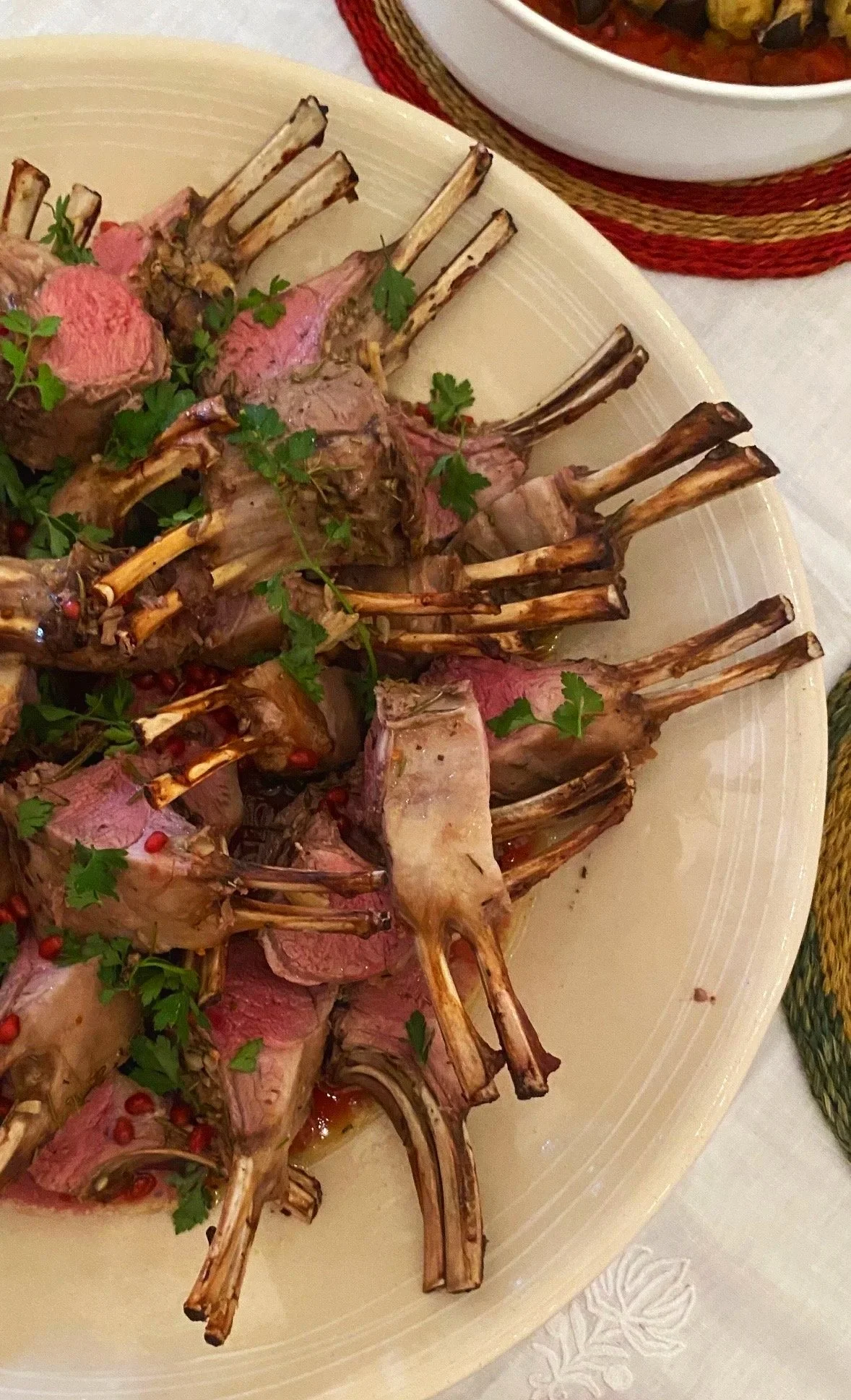 Plate of cooked lamb chops garnished with parsley and peppercorns, with a bowl of cooked vegetables in the background.