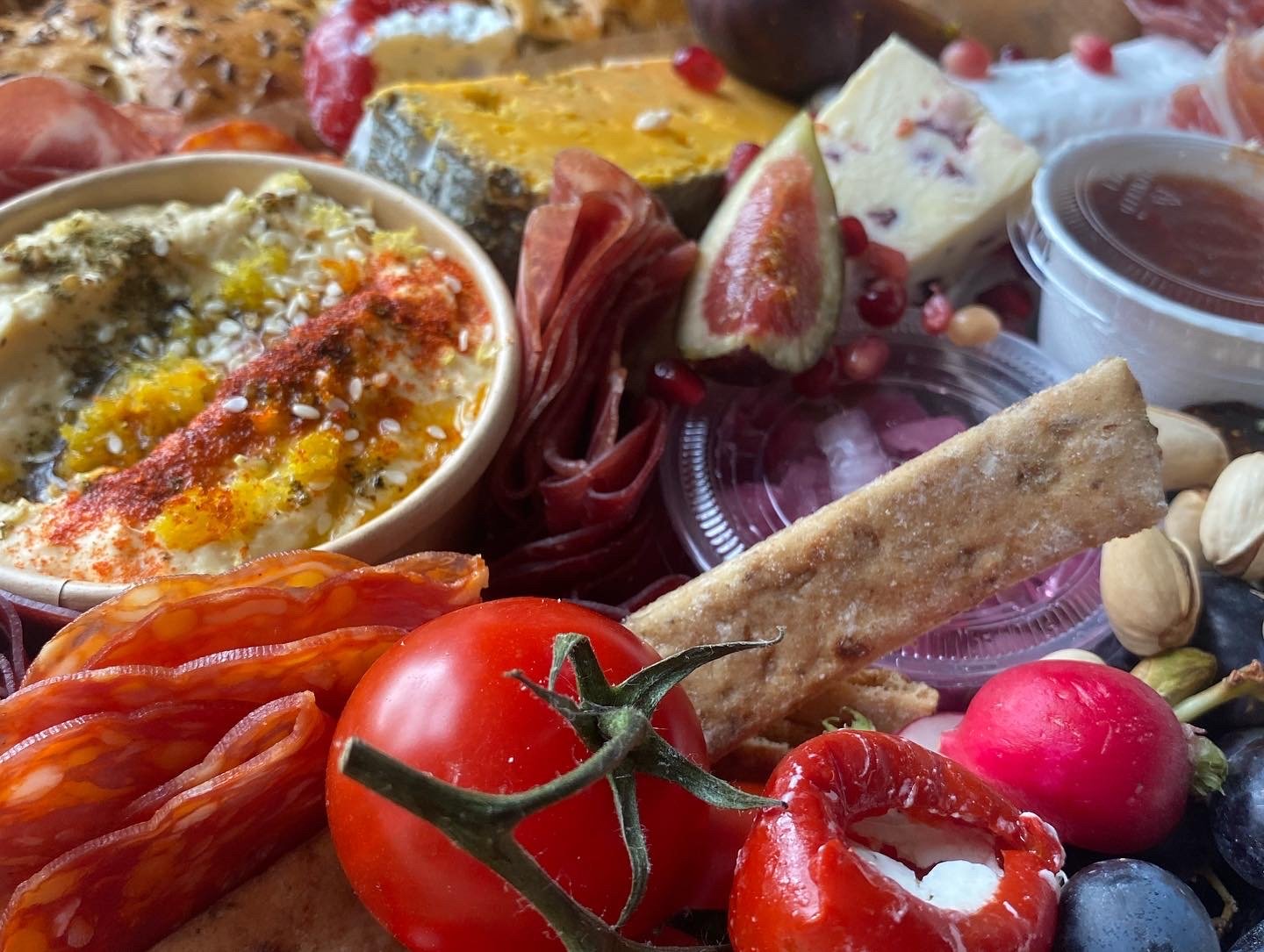 A cheese and vegetable platter featuring cherry tomatoes, radishes, sliced fig, nuts, dips, cheese and breadsticks.
