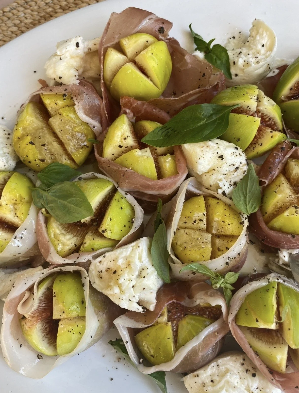 Siced figs wrapped in prosciutto with mozzarella, fresh basil leaves, and cracked black pepper.