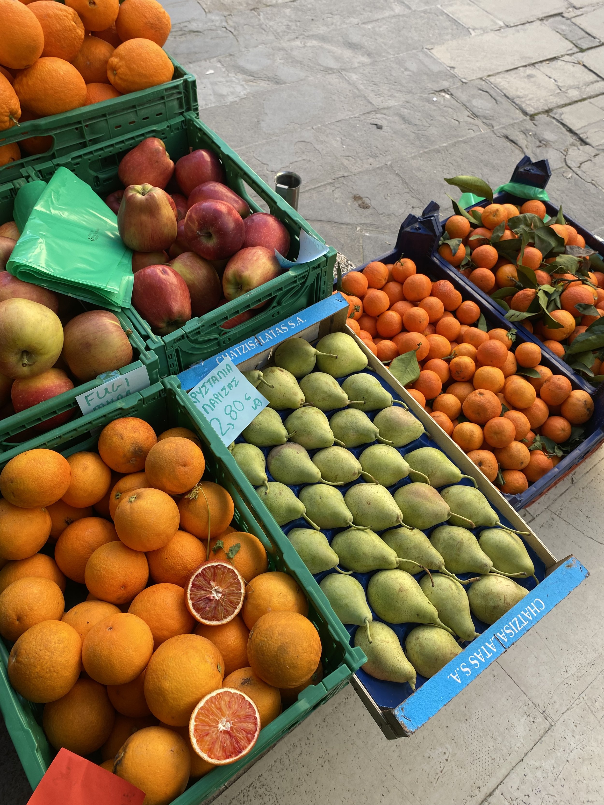 A display of fresh fruit including apples, oranges, tangerines, and pears at a market stall.