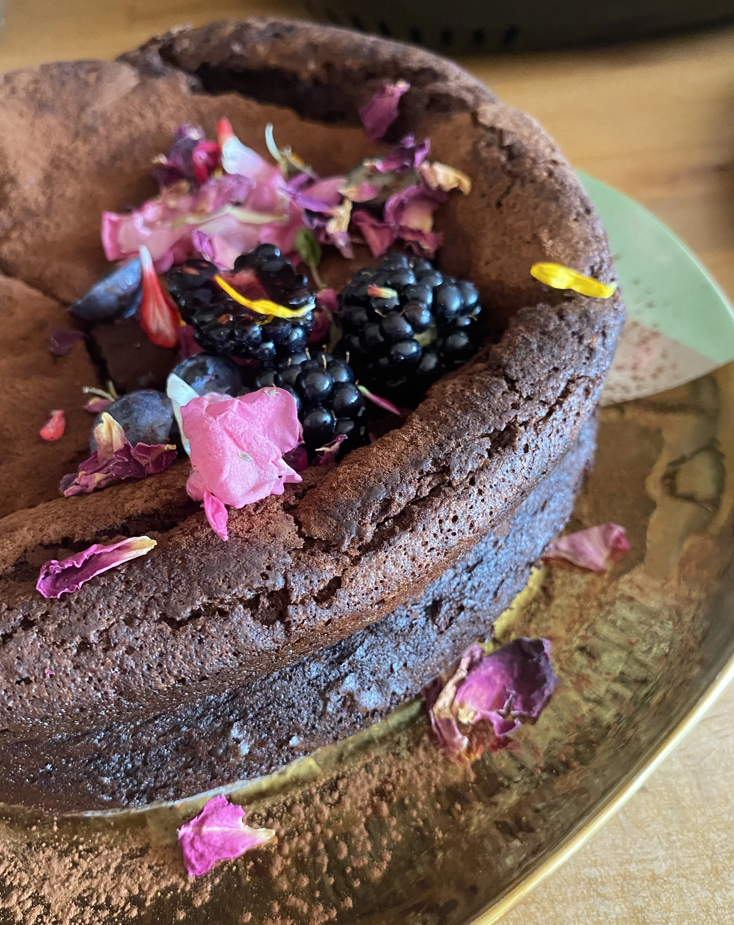 Chocolate cake decorated with berries and dried flower petals on top, placed in a glass dish.