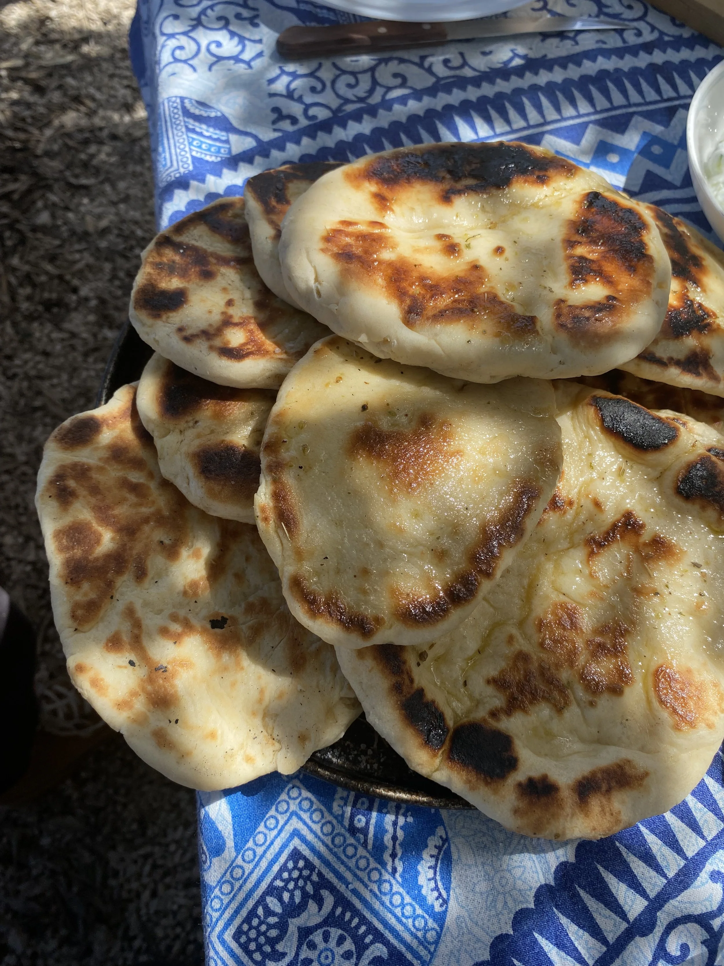 A plate of freshly baked flatbread with some charring, resting on a blue and white patterned cloth.
