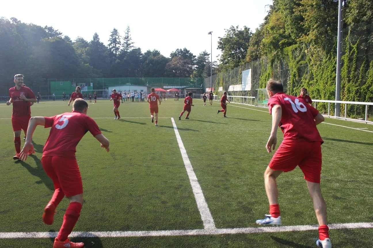 Fußballspieler in roten Uniformen beim Warm-up auf einem grünen Fußballfeld an einem sonnigen Tag.