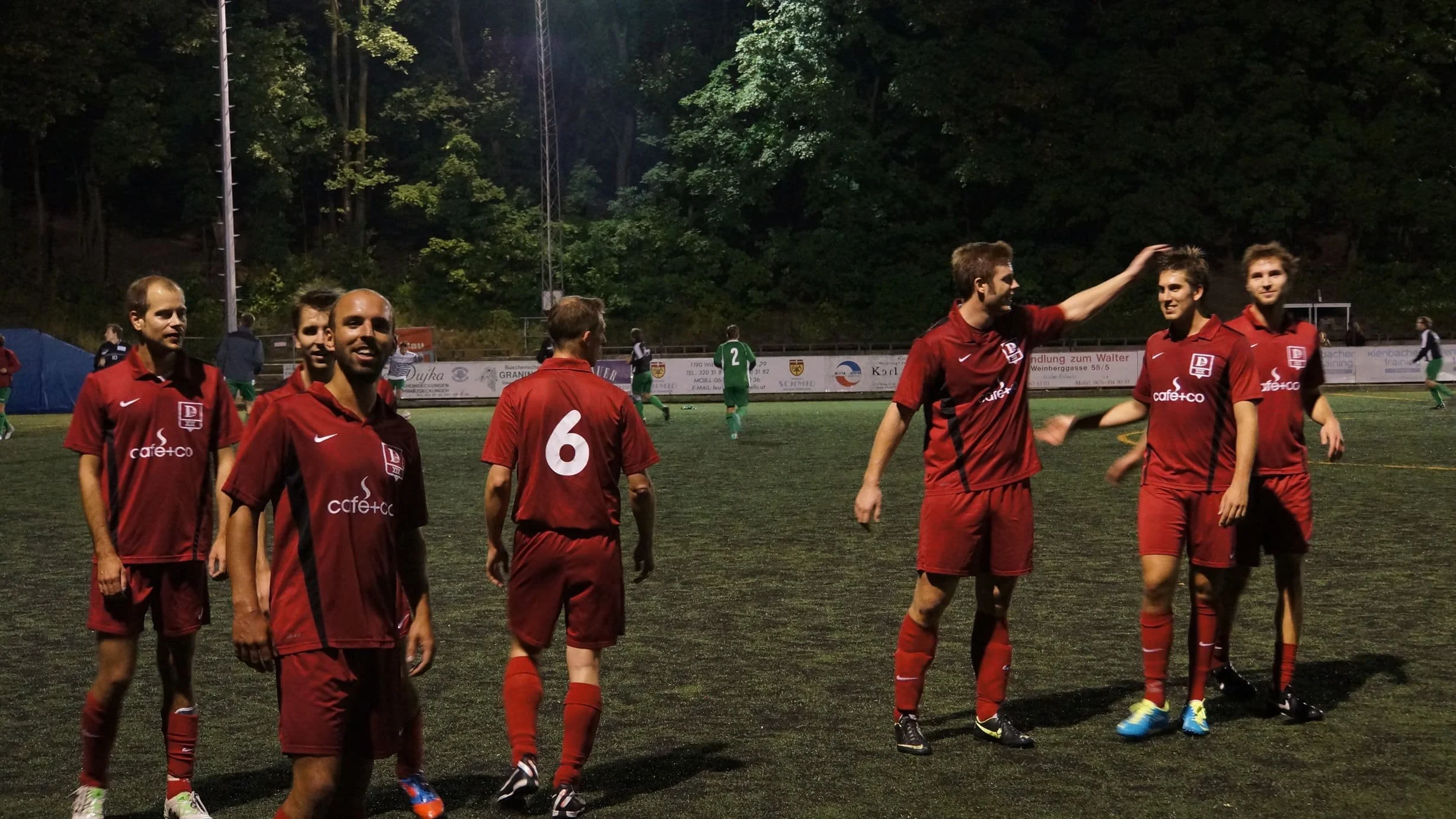 Fußballspieler in roten Trikots auf einem Fußballfeld nach einem Spiel, einige jubelnd, bei Nacht.