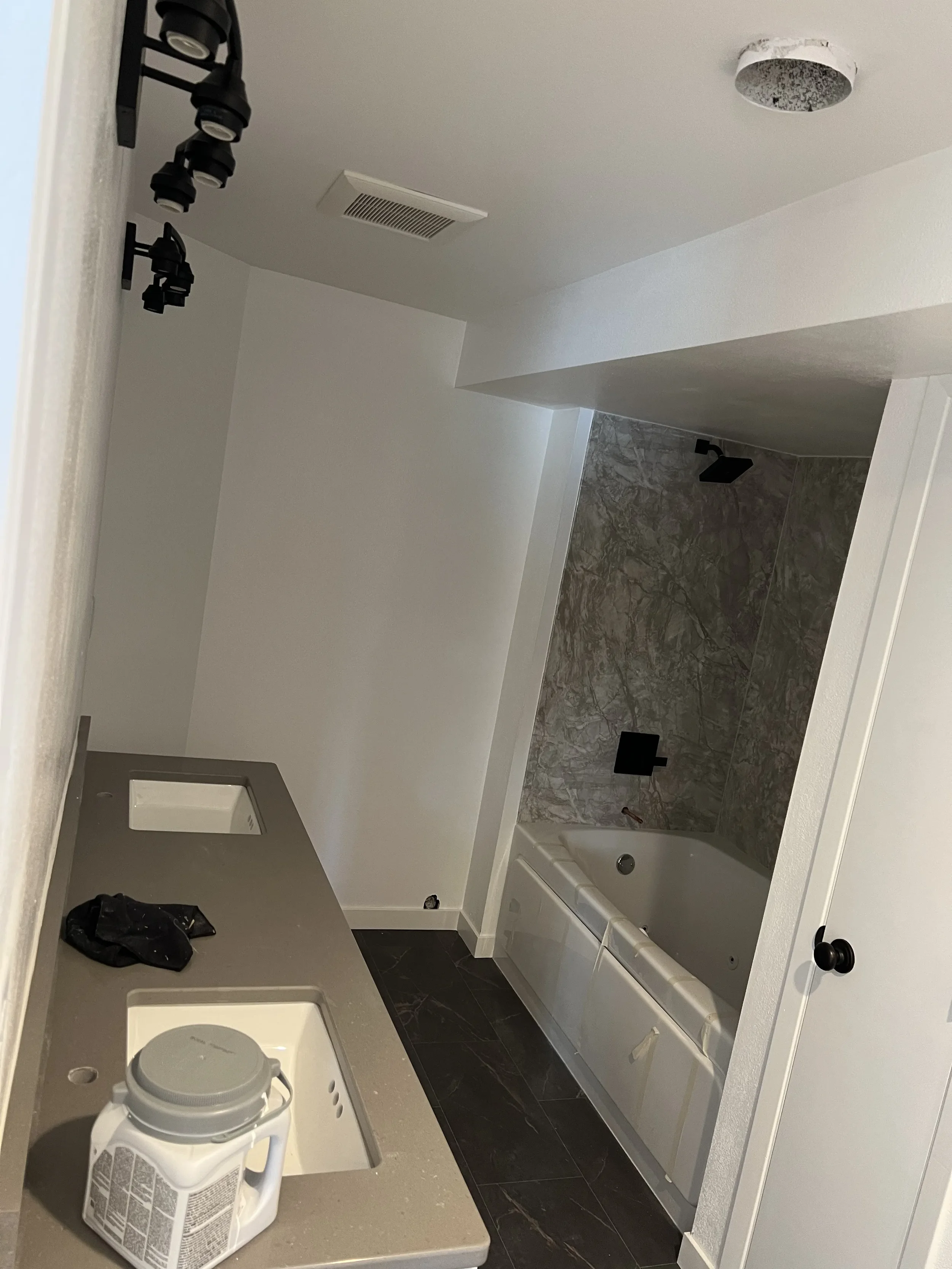 Bathroom under construction with a double sink vanity, a bathtub with marble tiles, and unpainted light-colored walls.