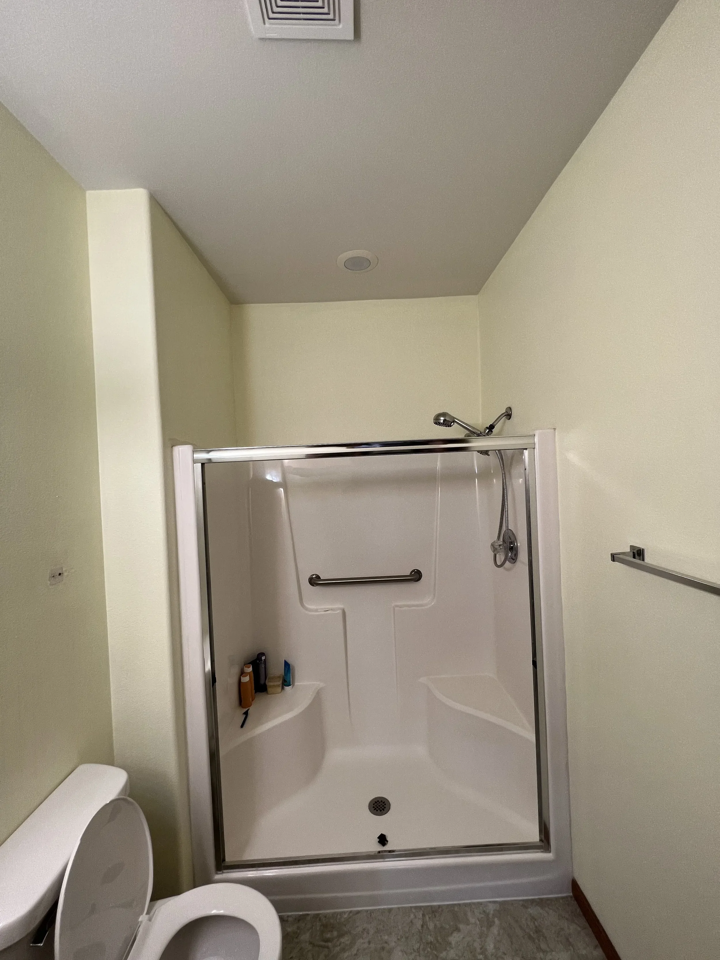 Bathroom with a walk-in shower, toilet with an open lid, towel bar on the wall, and toiletries placed on the shower shelf.
