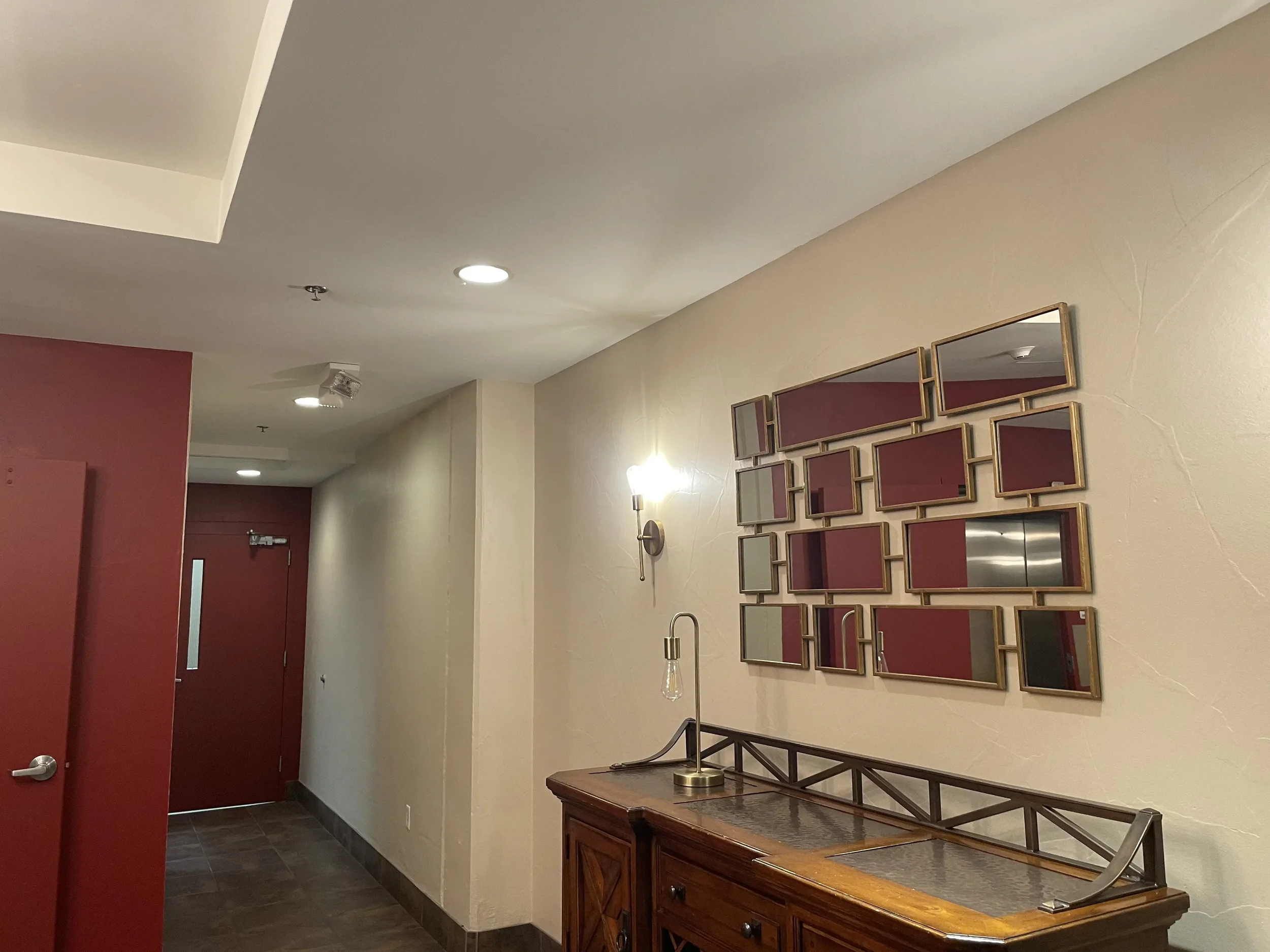 Interior hallway with a red door, wall mirror arrangement, and a wooden console table with a lamp and tabletop decor.