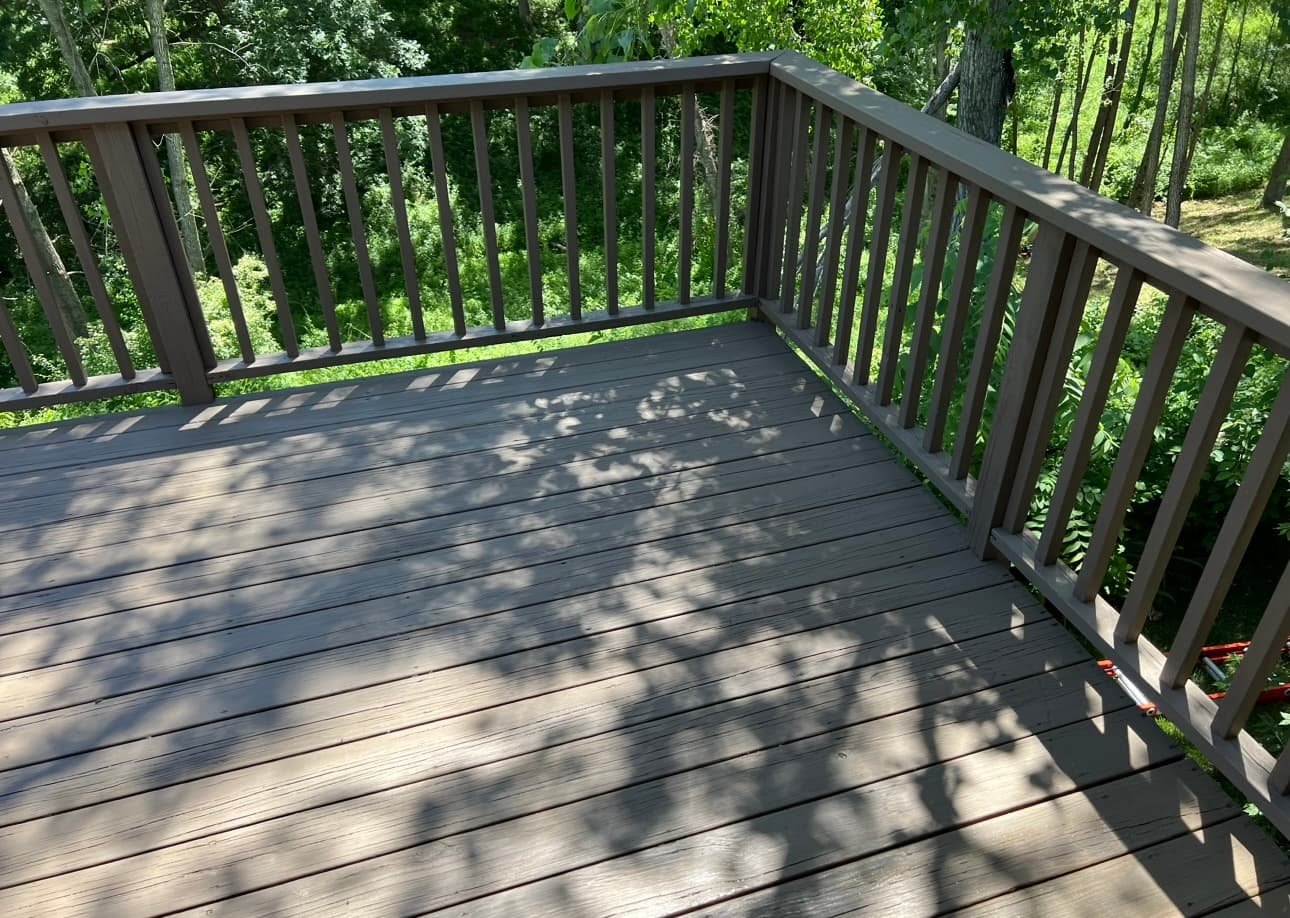 A wooden deck with railings overlooking a green, wooded area with trees and bushes.