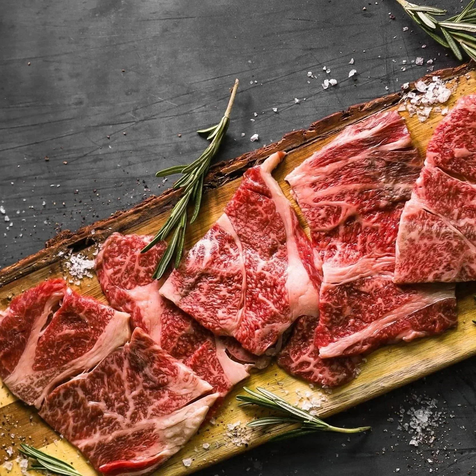 Raw marbled beef steaks with rosemary and coarse salt on a wooden cutting board.