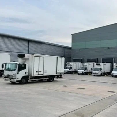 Several white delivery trucks parked in a lot near large industrial buildings.