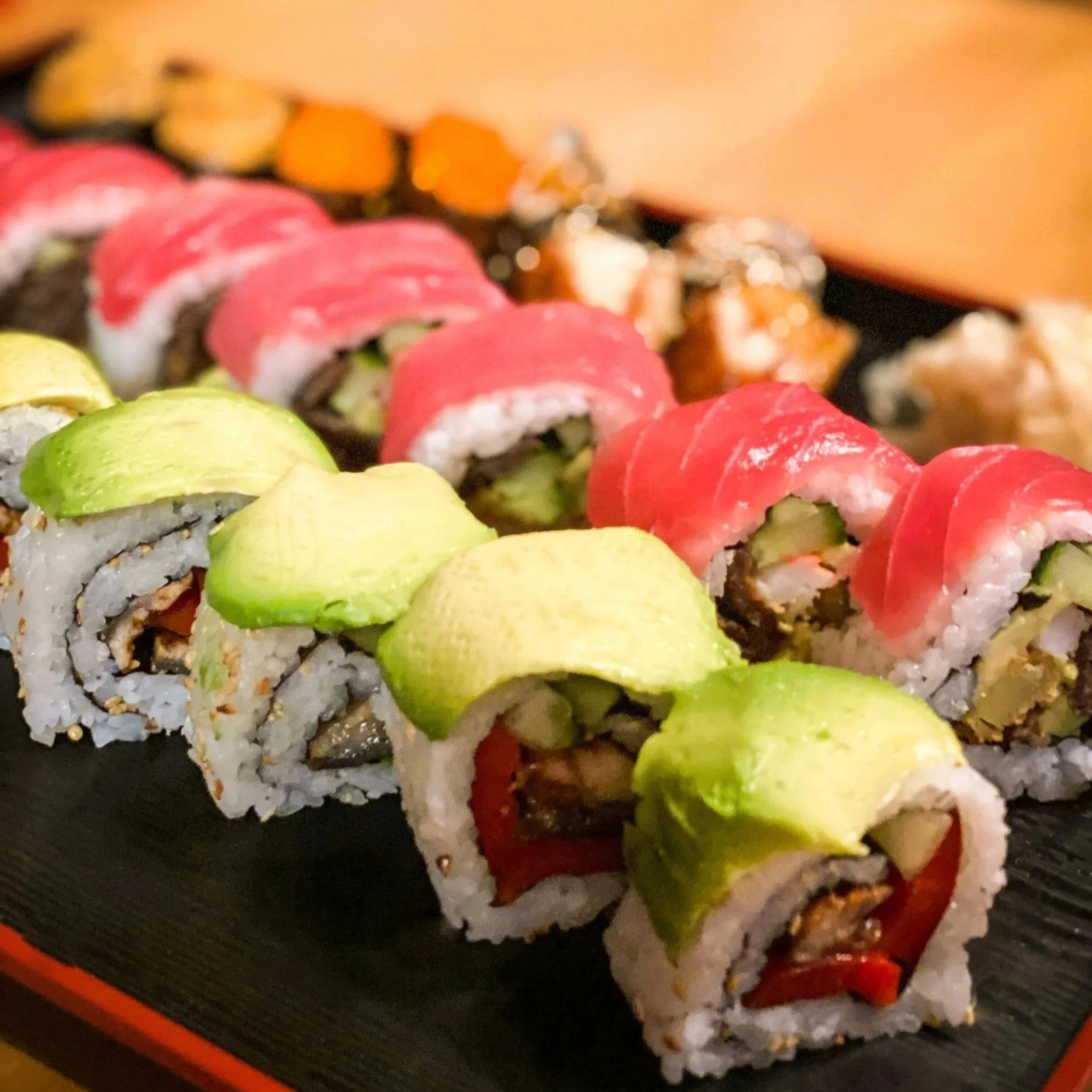 Close-up of sushi rolls in a black and orange sushi tray with vibrant pink, green, and orange ingredients.