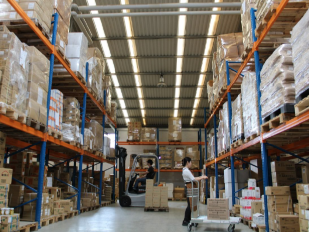 Warehouse with tall shelves stocked with boxes, a forklift, and workers moving items.
